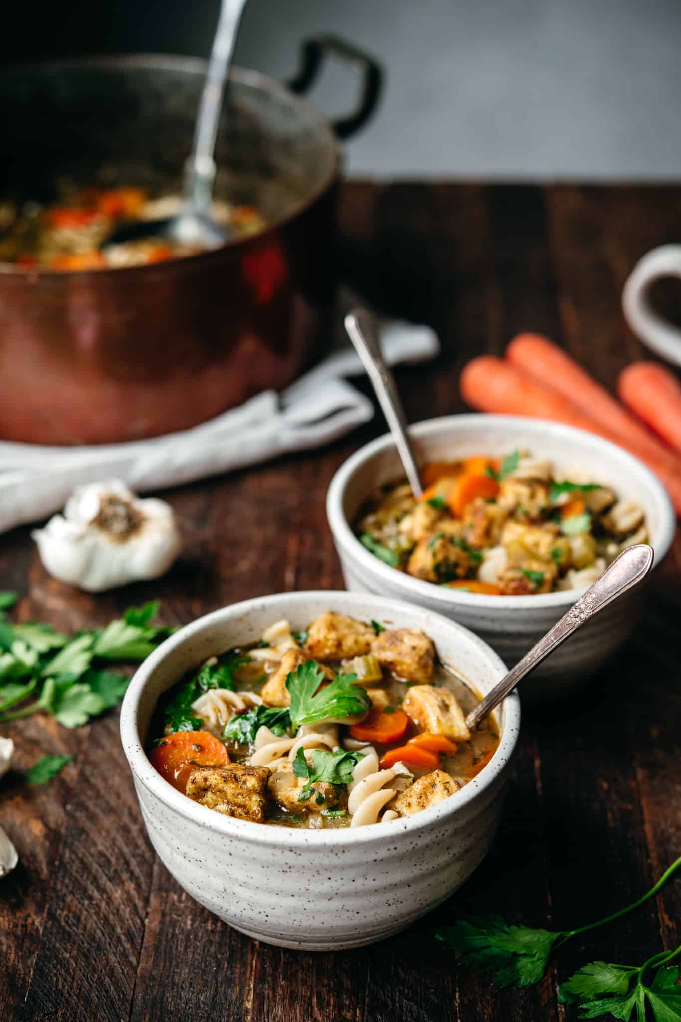 side view of two bowls of vegan chicken noodle soup in on wood table