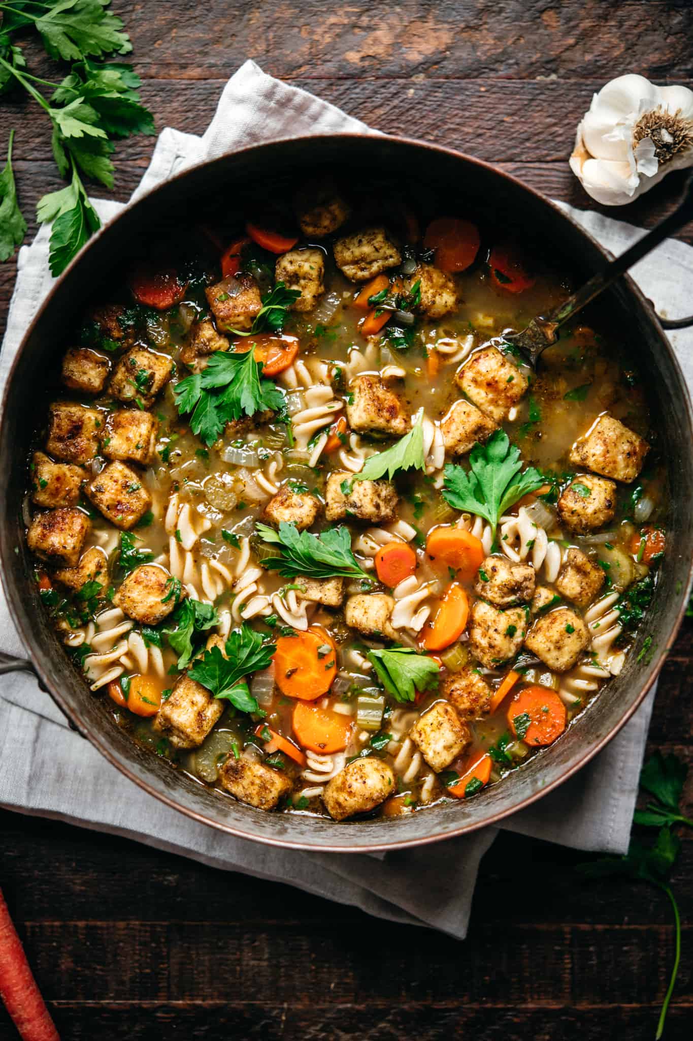 overhead view of vegan chicken noodle soup with crispy tofu in large copper pot