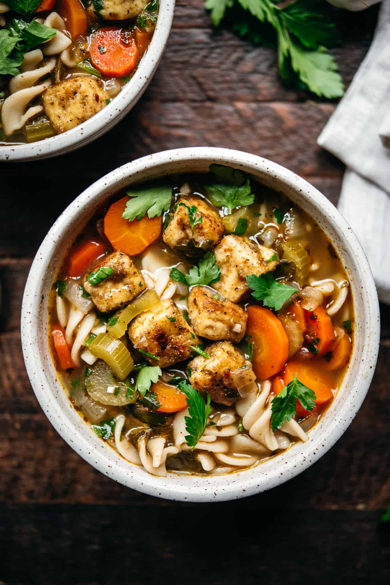 close up overhead view of vegan chicken noodle tofu soup in white bowl