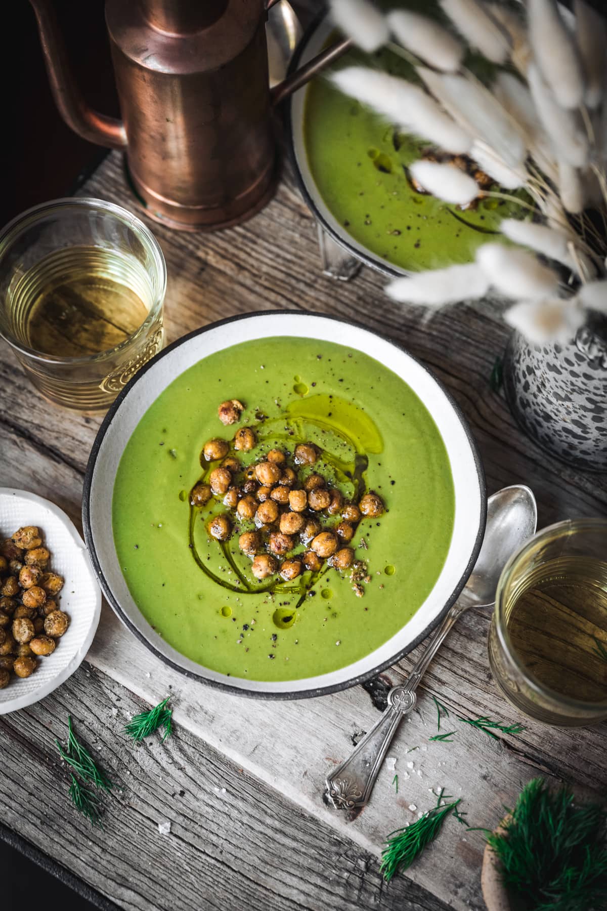 overhead view of creamy vegan broccoli spinach soup on wood table with crispy chickpeas