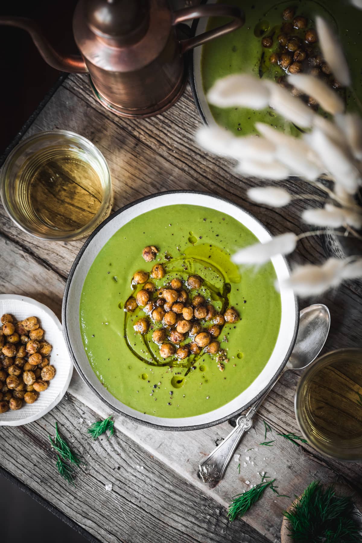 overhead view of creamy vegan broccoli spinach soup on wood table with crispy chickpeas