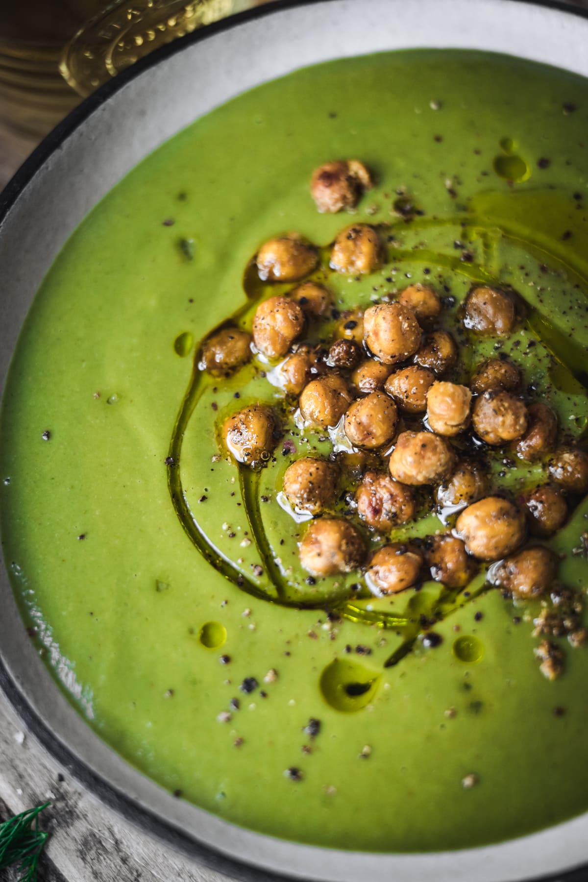 close up view of vegan broccoli potato spinach soup topped with olive oil and crispy chickpeas