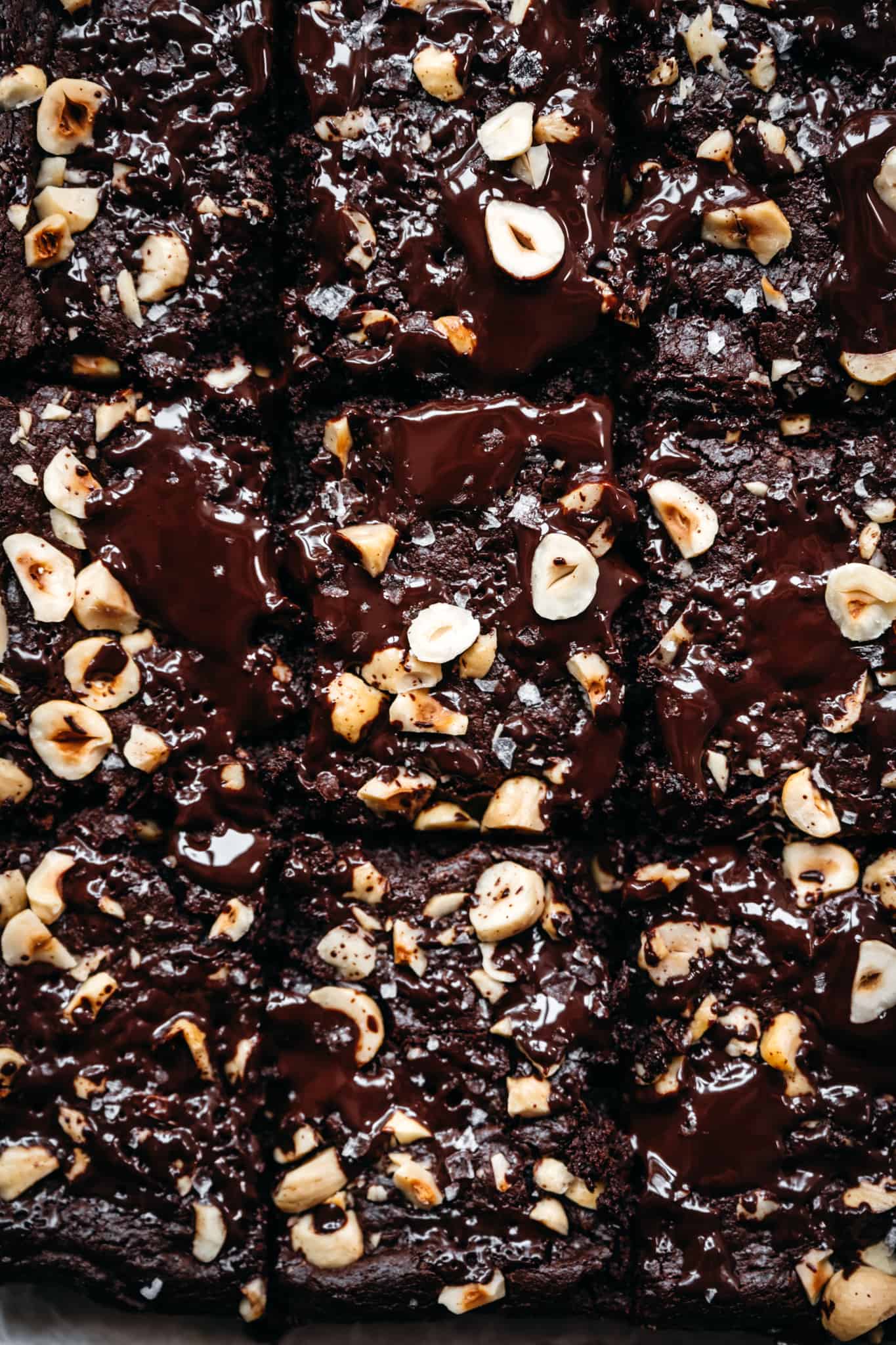 close up overhead view of tahini brownies topped with dark chocolate, hazelnuts and flaky salt