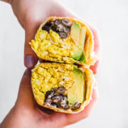 close up of person holding vegan breakfast burrito cut in half.