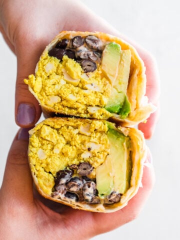 close up of person holding vegan breakfast burrito cut in half.