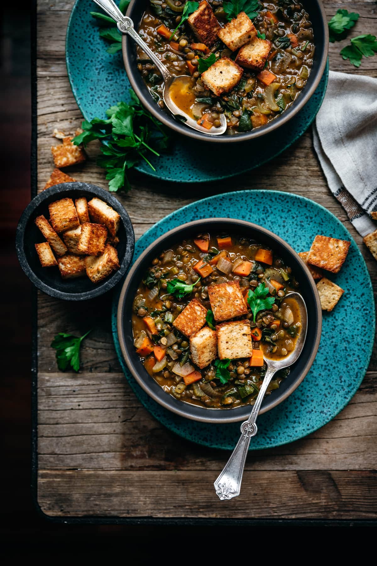 overhead view of vegan lentil stew with garlic croutons on wood table