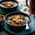 Vegan lentil stew from a 45 degree angle, garnished with a spoon and croutons.