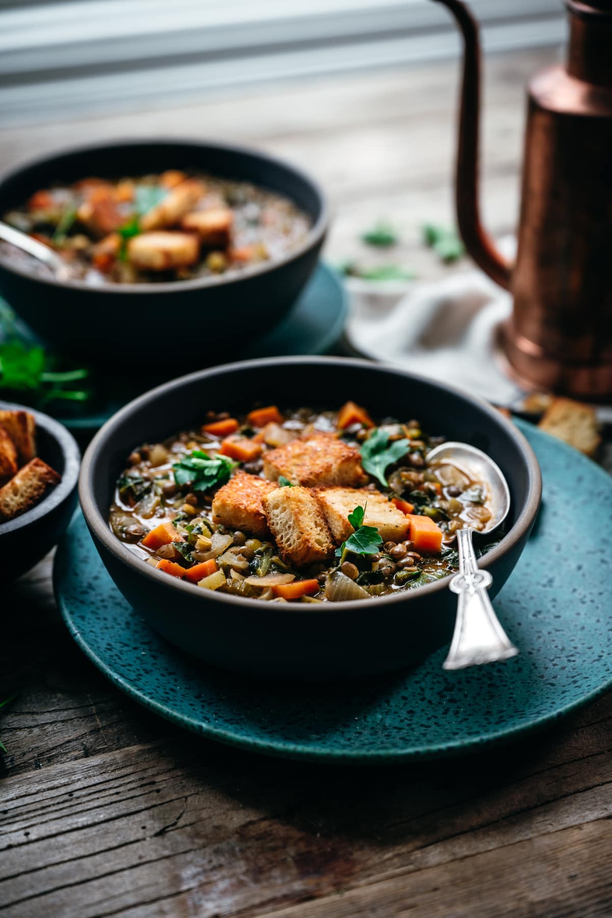 backlit side view of vegan lentil vegetable stew in blue bowl on wood table