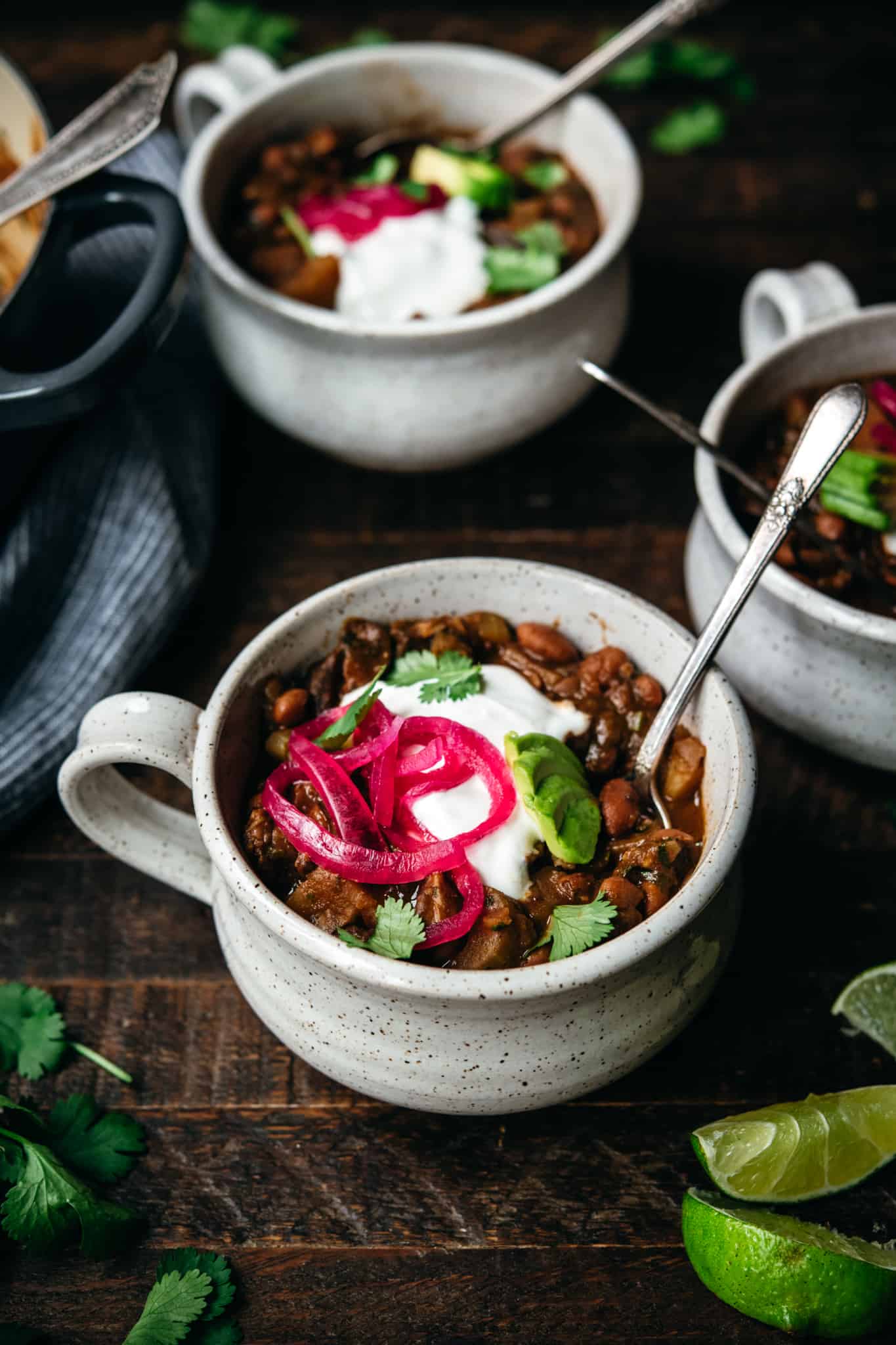 side view of vegan pinto bean chili with sour cream and pickled onions in ceramic bowl with spoon