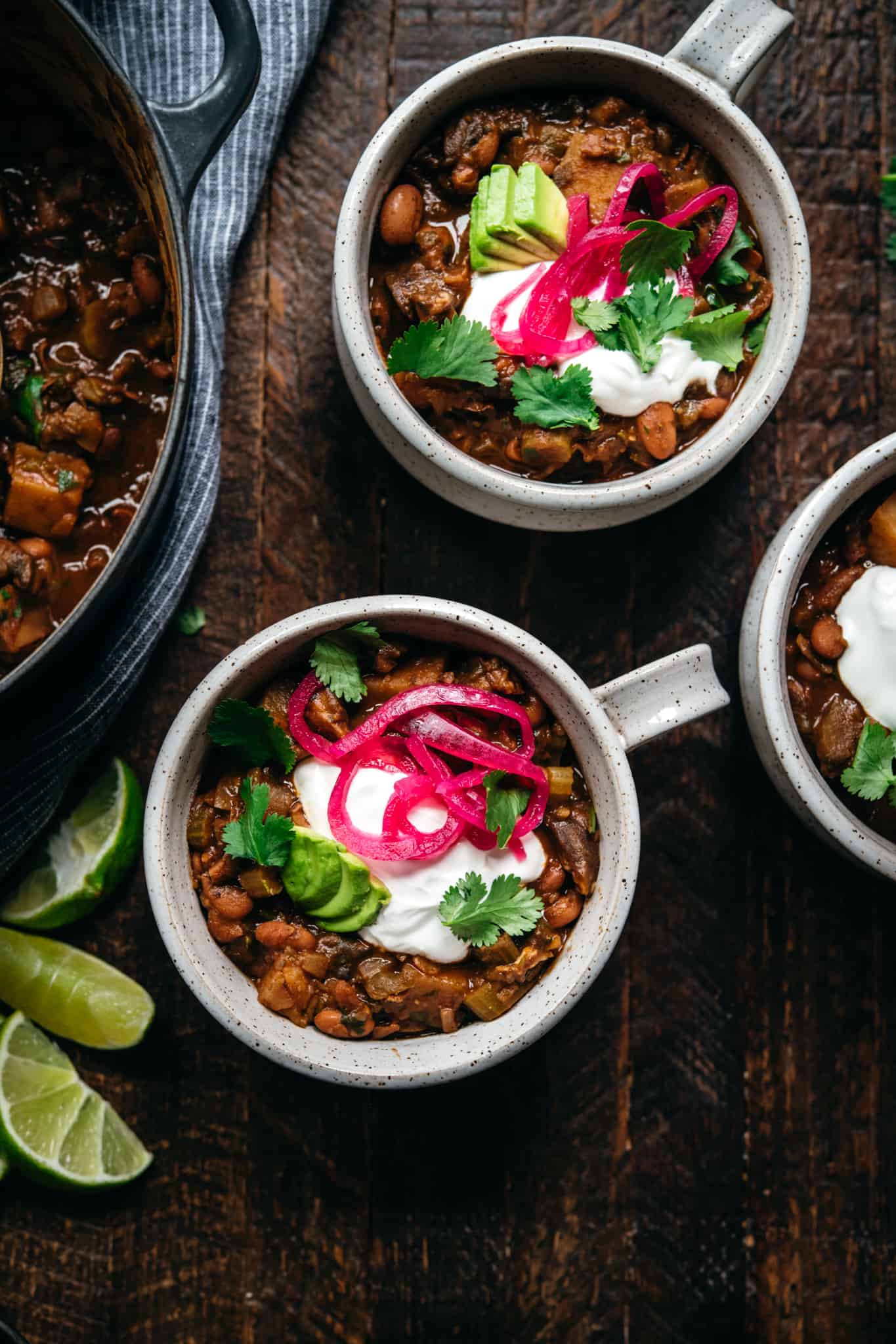 overhead view of vegan pinto bean chili in white ceramic bowls on wood background