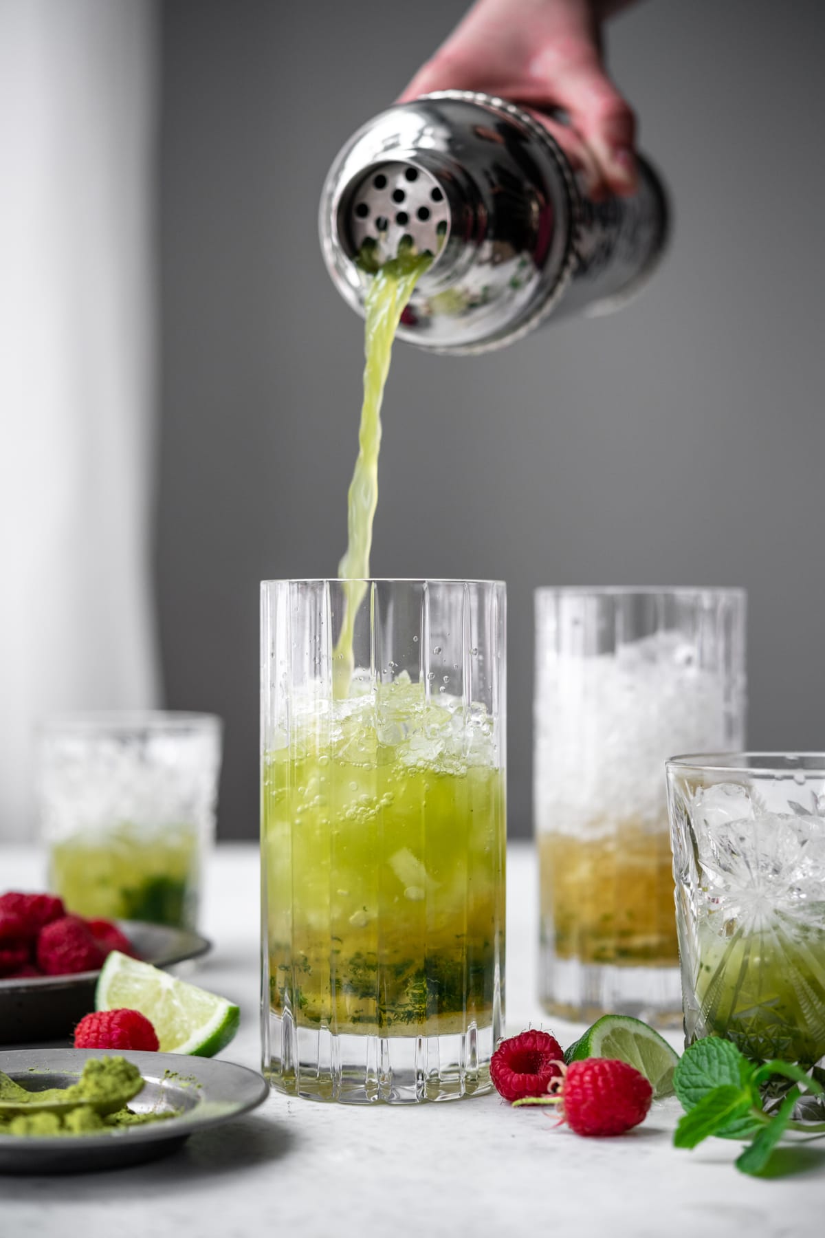 side view of pouring matcha mojito into highball glass from cocktail shaker