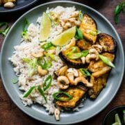 Overhead view of miso eggplant with lime wedges, rice, and cashews.