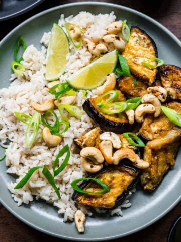 Overhead view of miso eggplant with lime wedges, rice, and cashews.