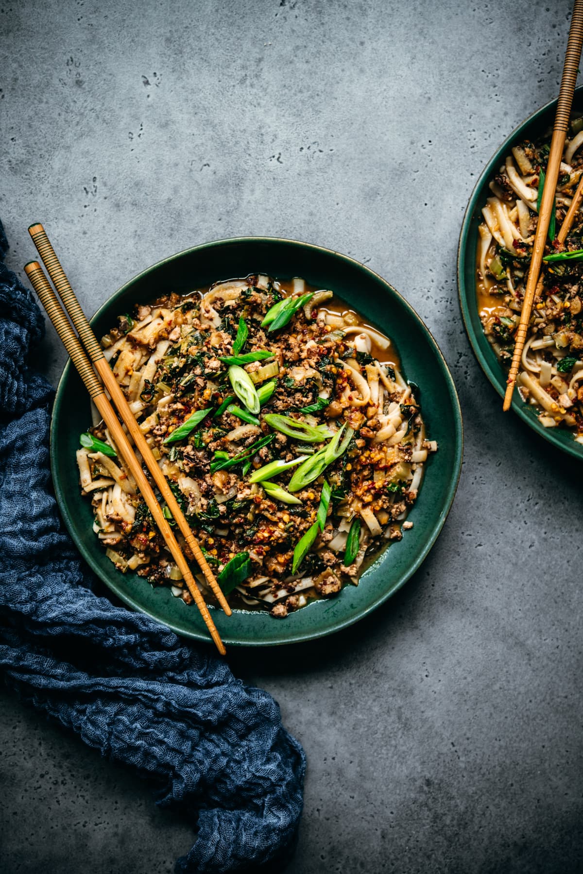 overhead view of vegan dan dan noodles with scallions and chopsticks in blue bowl