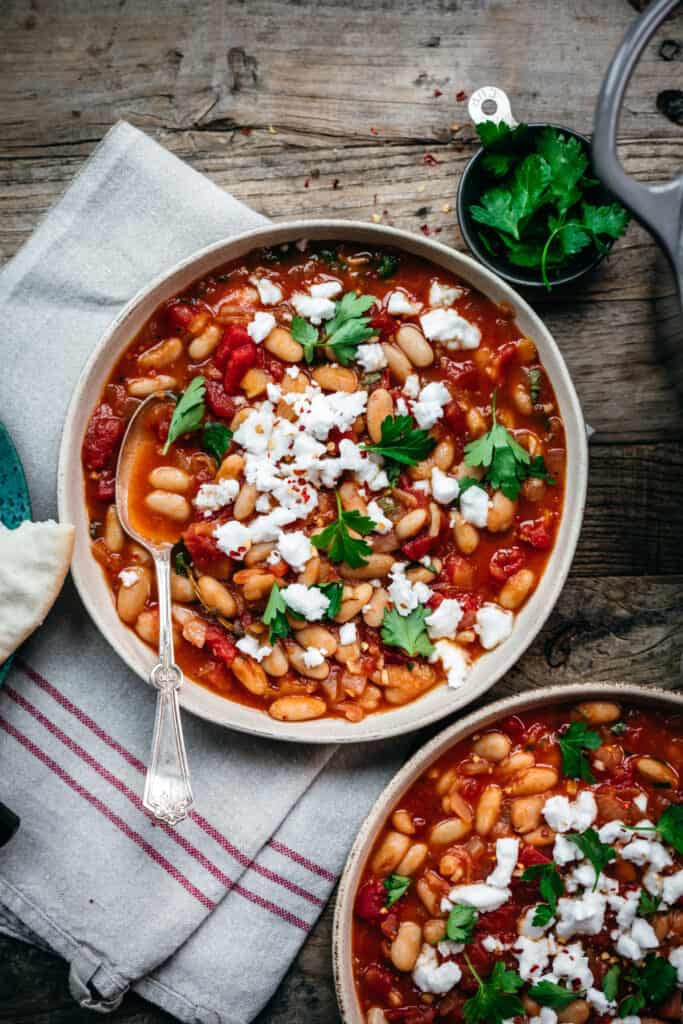 overhead view of vegan tomato white bean stew with feta and parsley in white bowl with spoon