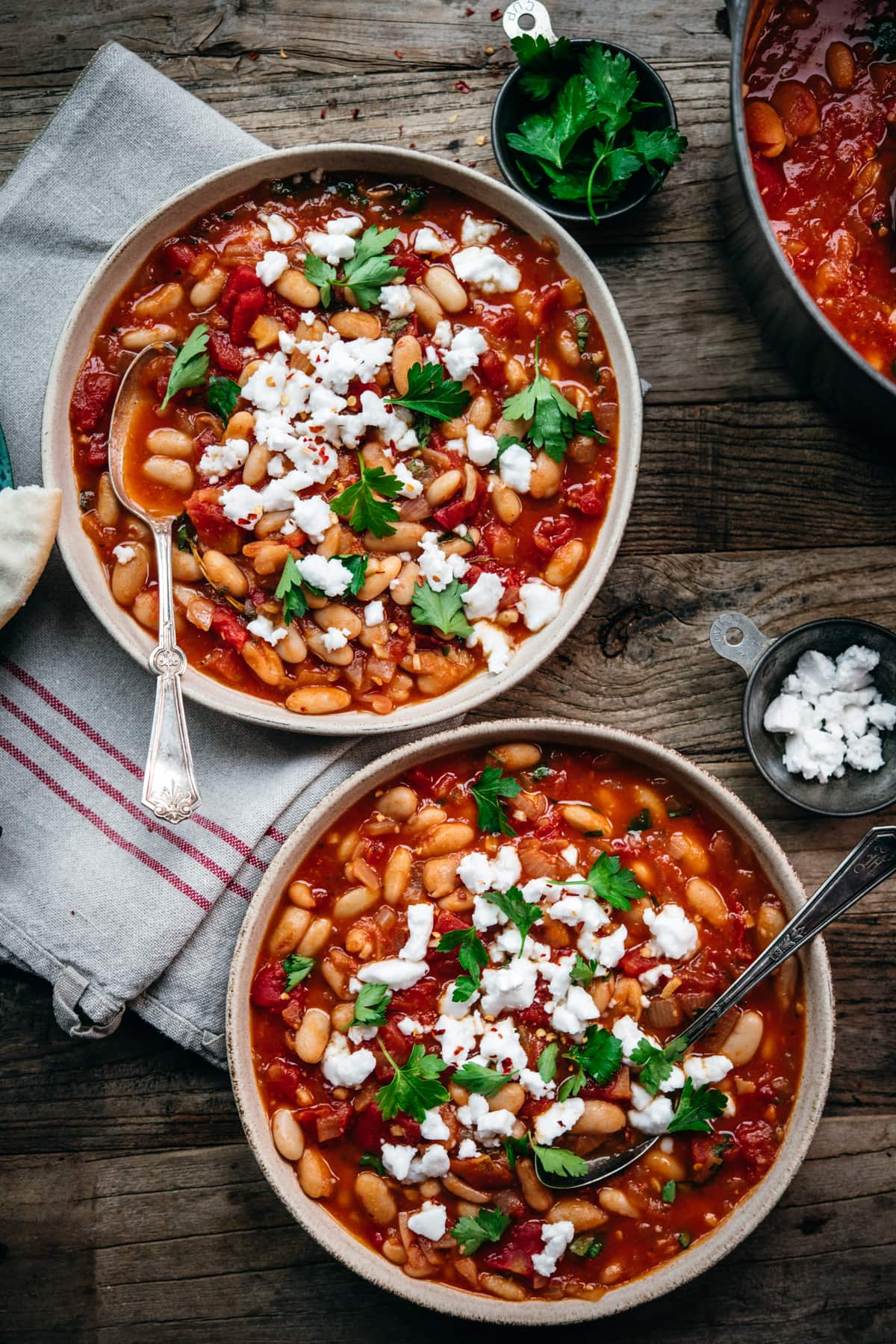 overhead view of two bowls of vegan white bean tomato stew with feta and parsley