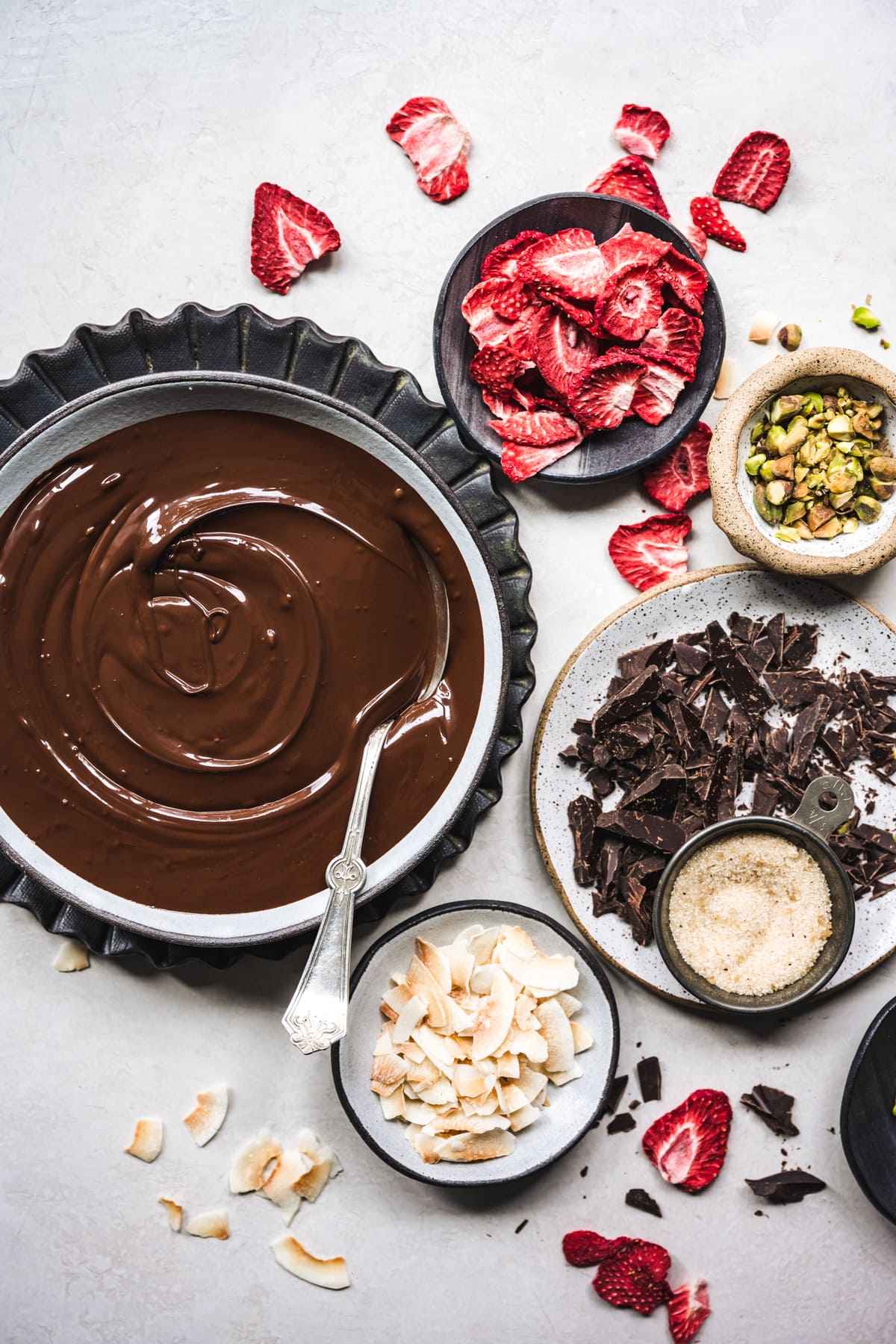 overhead view of ingredients for dark chocolate bark with strawberries, coconut and pistachios