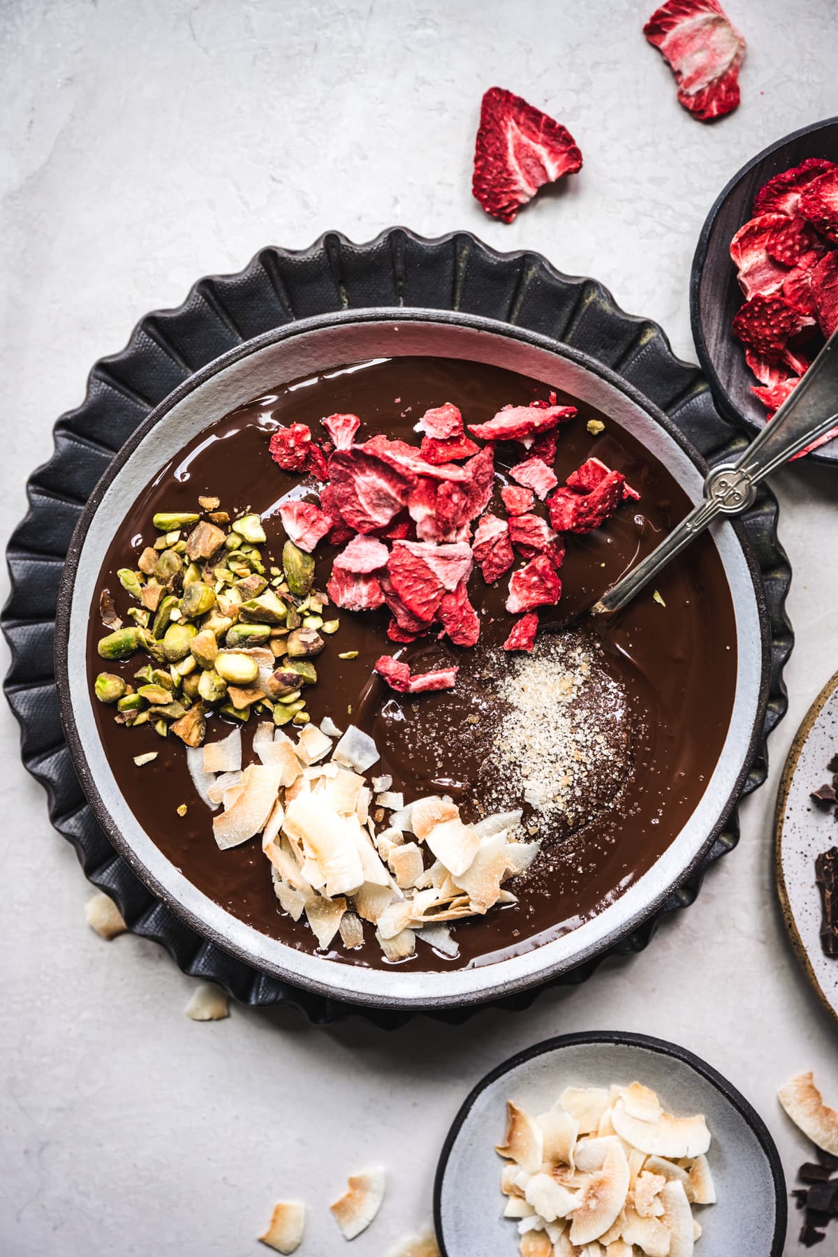 overhead view of melted dark chocolate with strawberries, pistachios and coconut