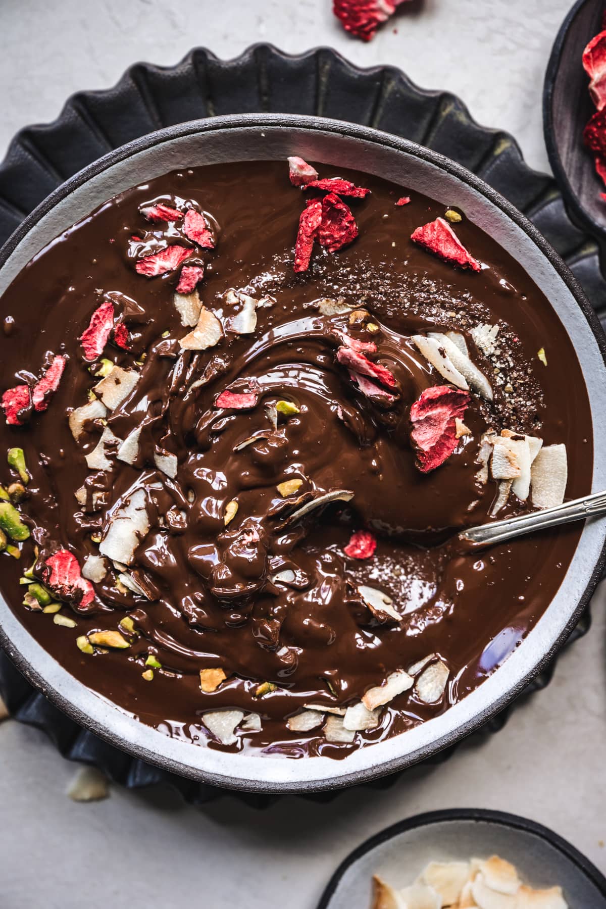 overhead view of melted dark chocolate with strawberries, pistachios and coconut