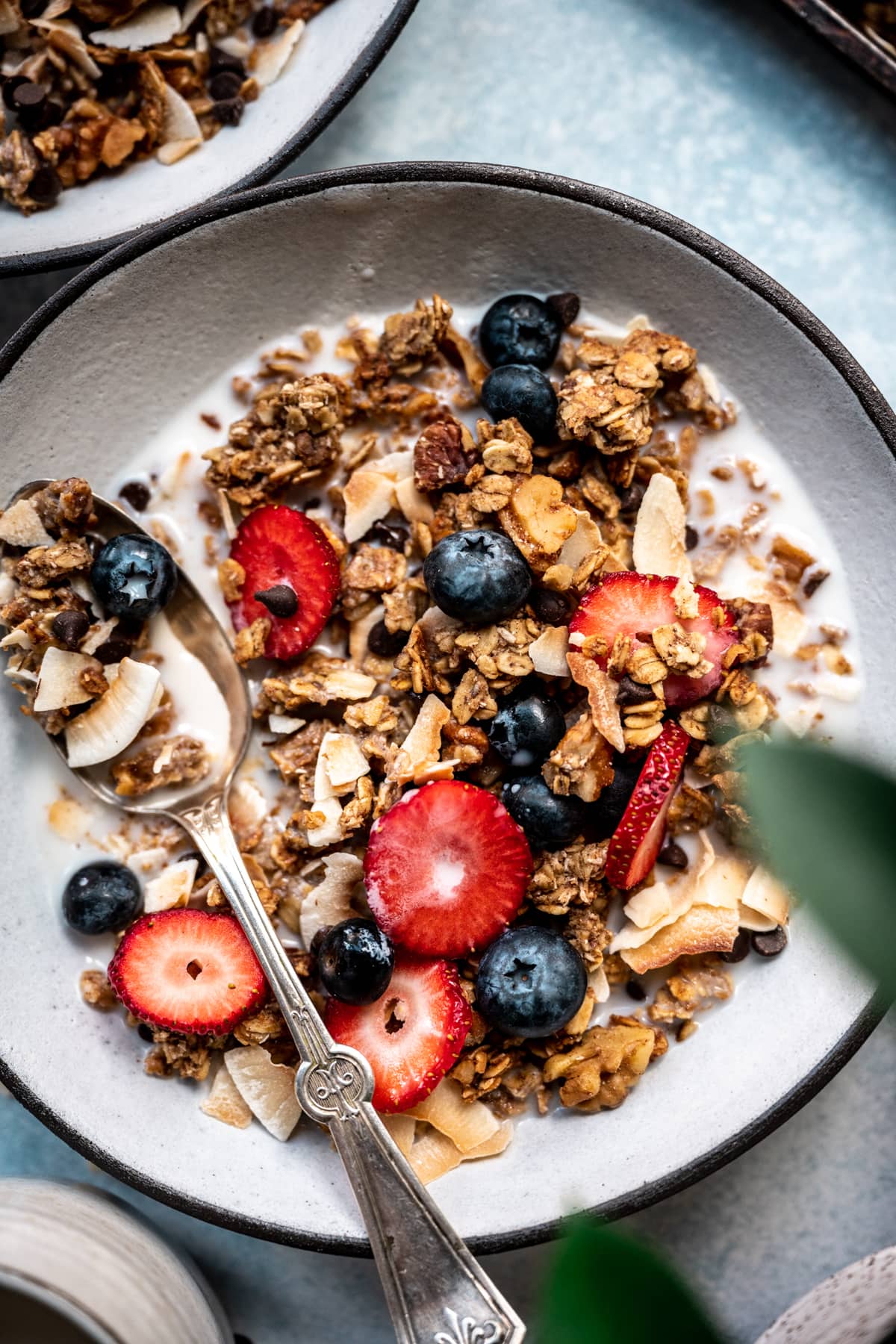 close up overhead view of banana bread granola in bowl with milk, sliced strawberries and blueberries