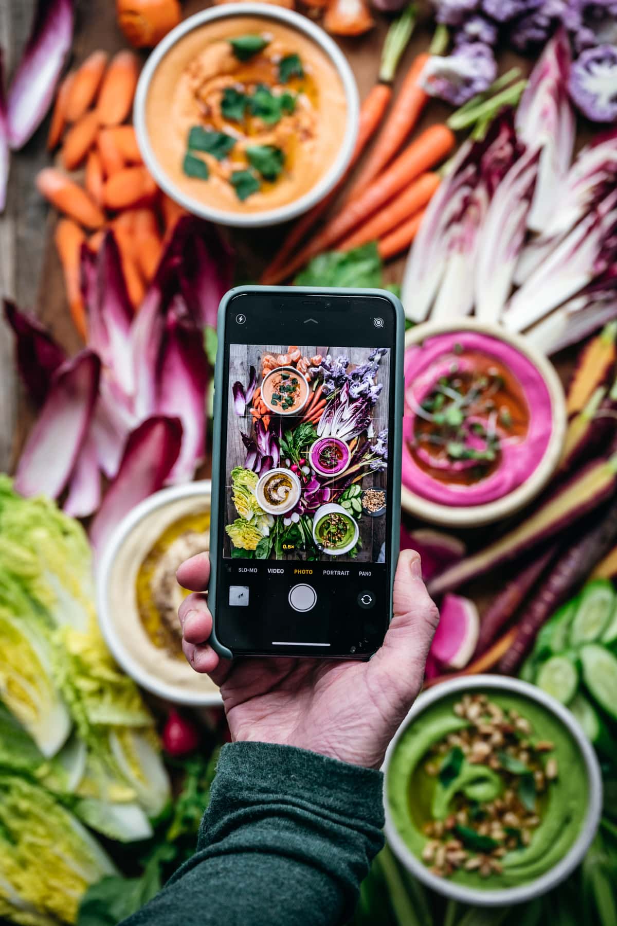 overhead view of person holding phone over colorful hummus platter