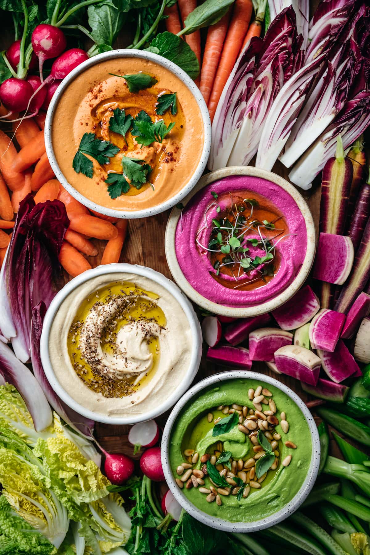 overhead view of homemade hummus 4 ways with colorful vegetables on a platter