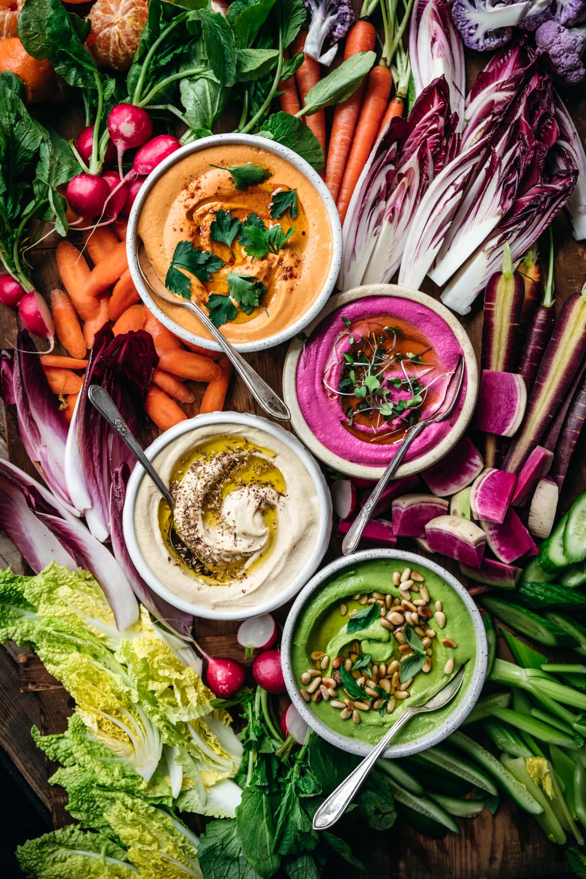 overhead view of homemade hummus 4 ways with colorful vegetables on a platter