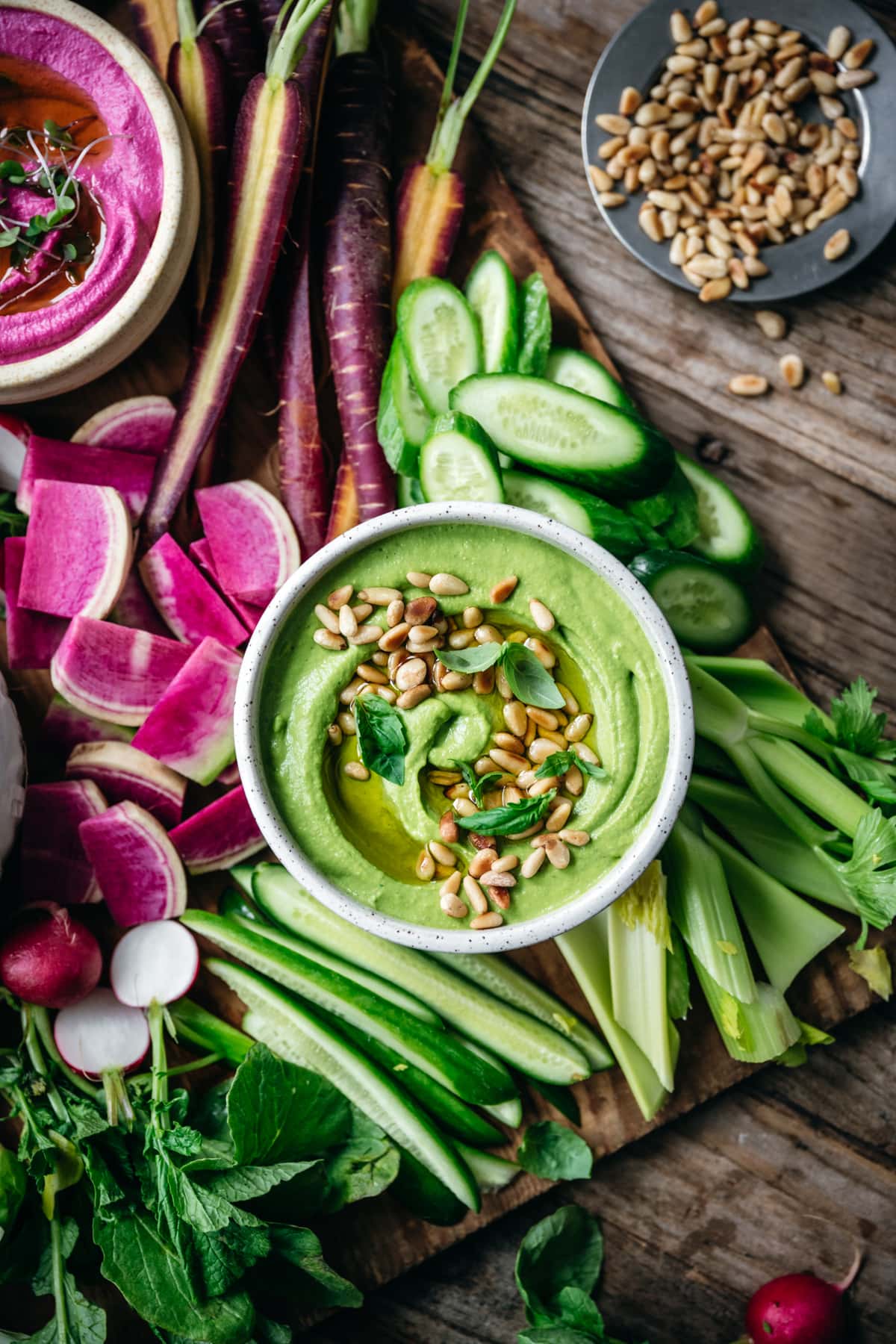 overhead view of pesto hummus in a bowl with pine nuts and basil