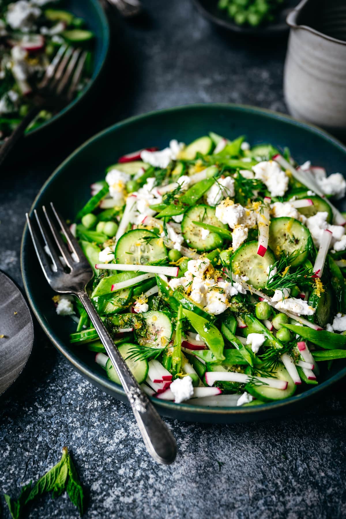 close up side view of snow pea salad with radishes, cucumber and vegan feta in blue bowl