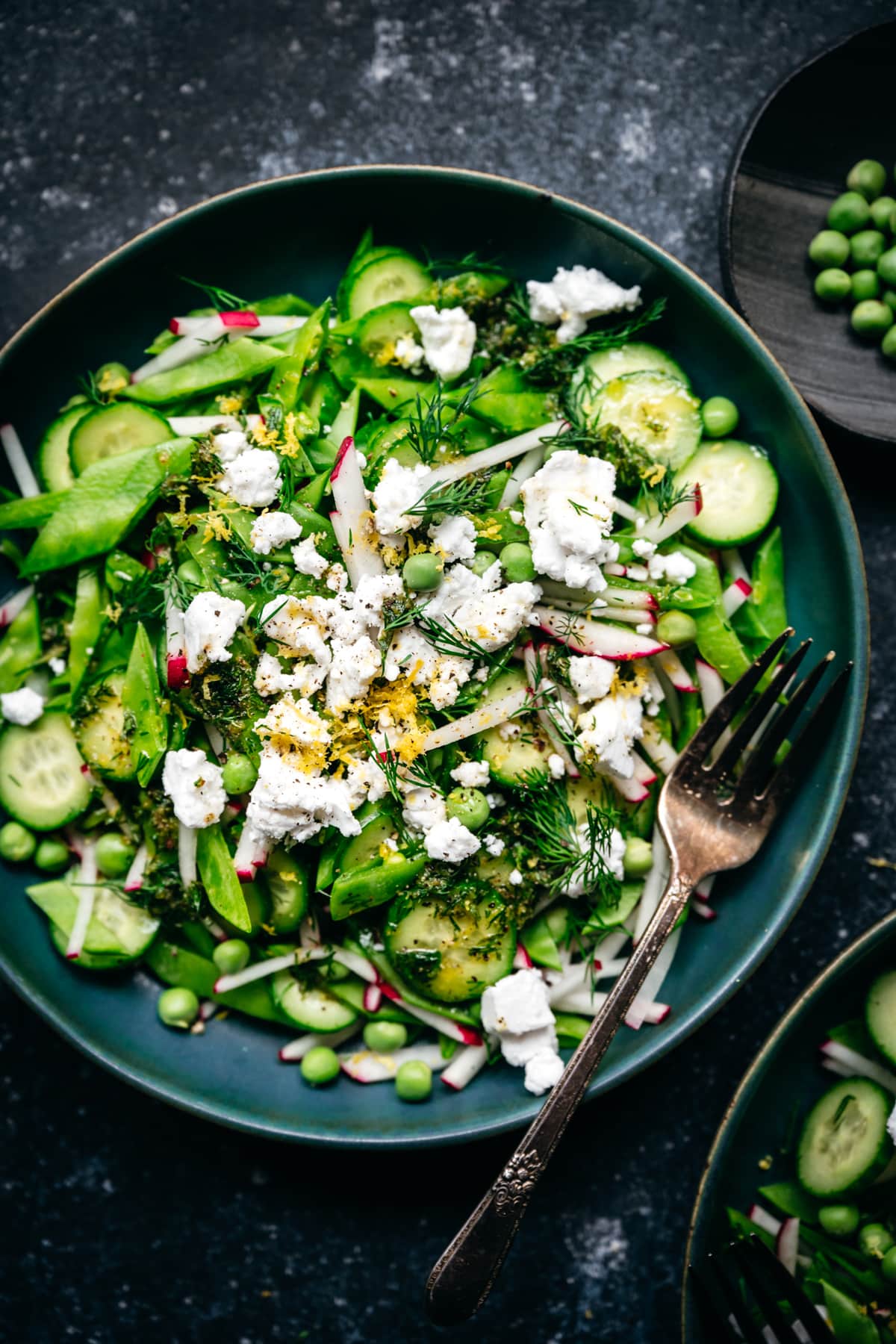 close up overhead view of snow pea salad with radishes, cucumber and vegan feta in blue bowl