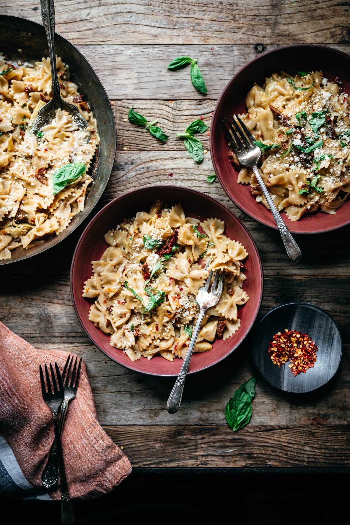 close up overhead view of vegan sun-dried tomato pasta in red bowls on wood table