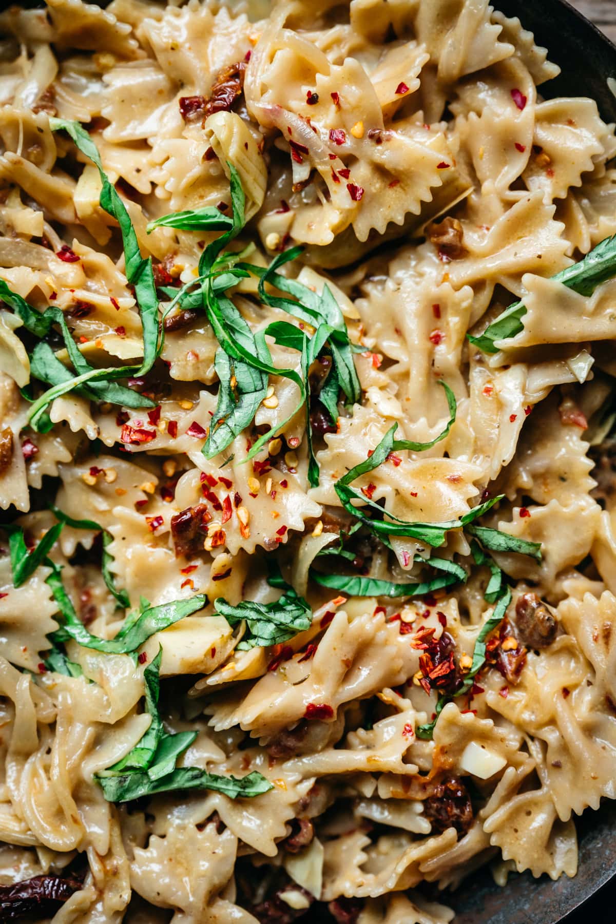 overhead view of vegan sun-dried tomato pasta with basil and red pepper flakes in pan