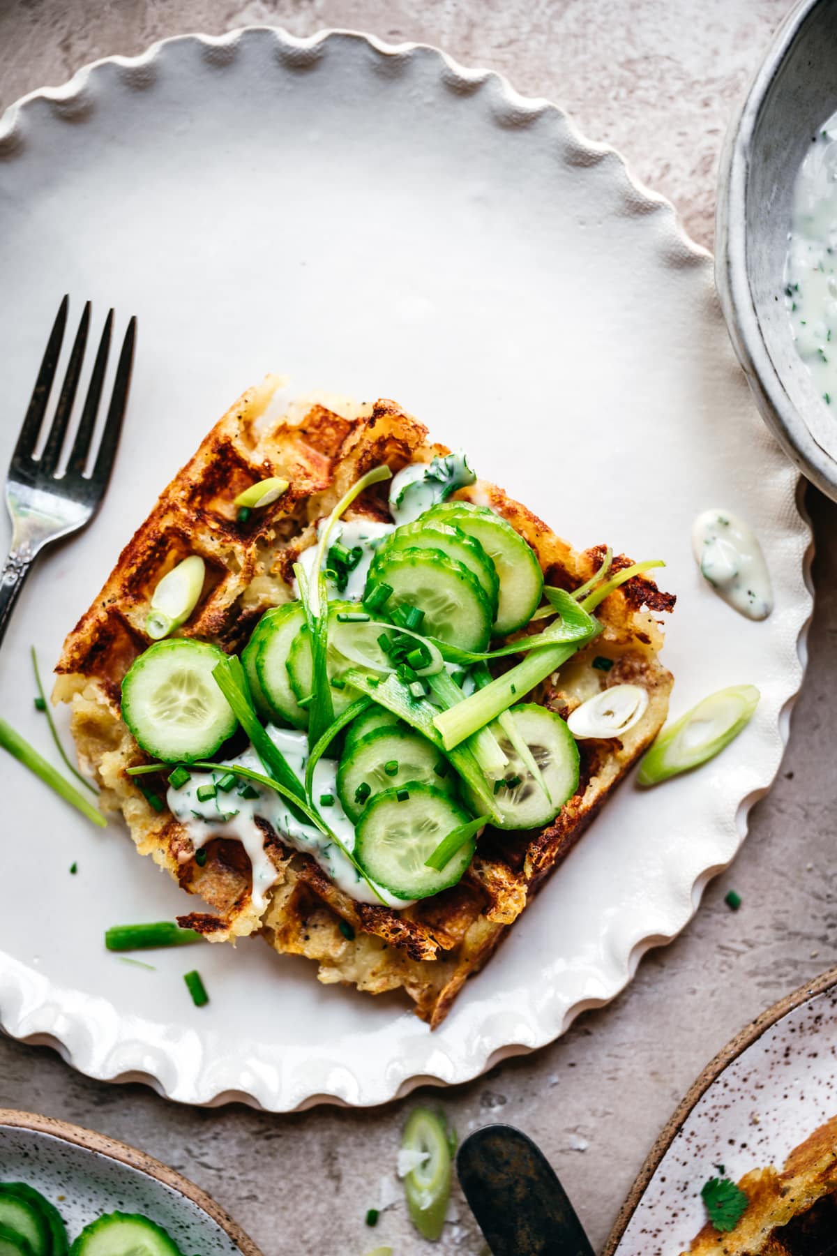 overhead view of mashed potato waffle topped with yogurt sauce and cucumbers