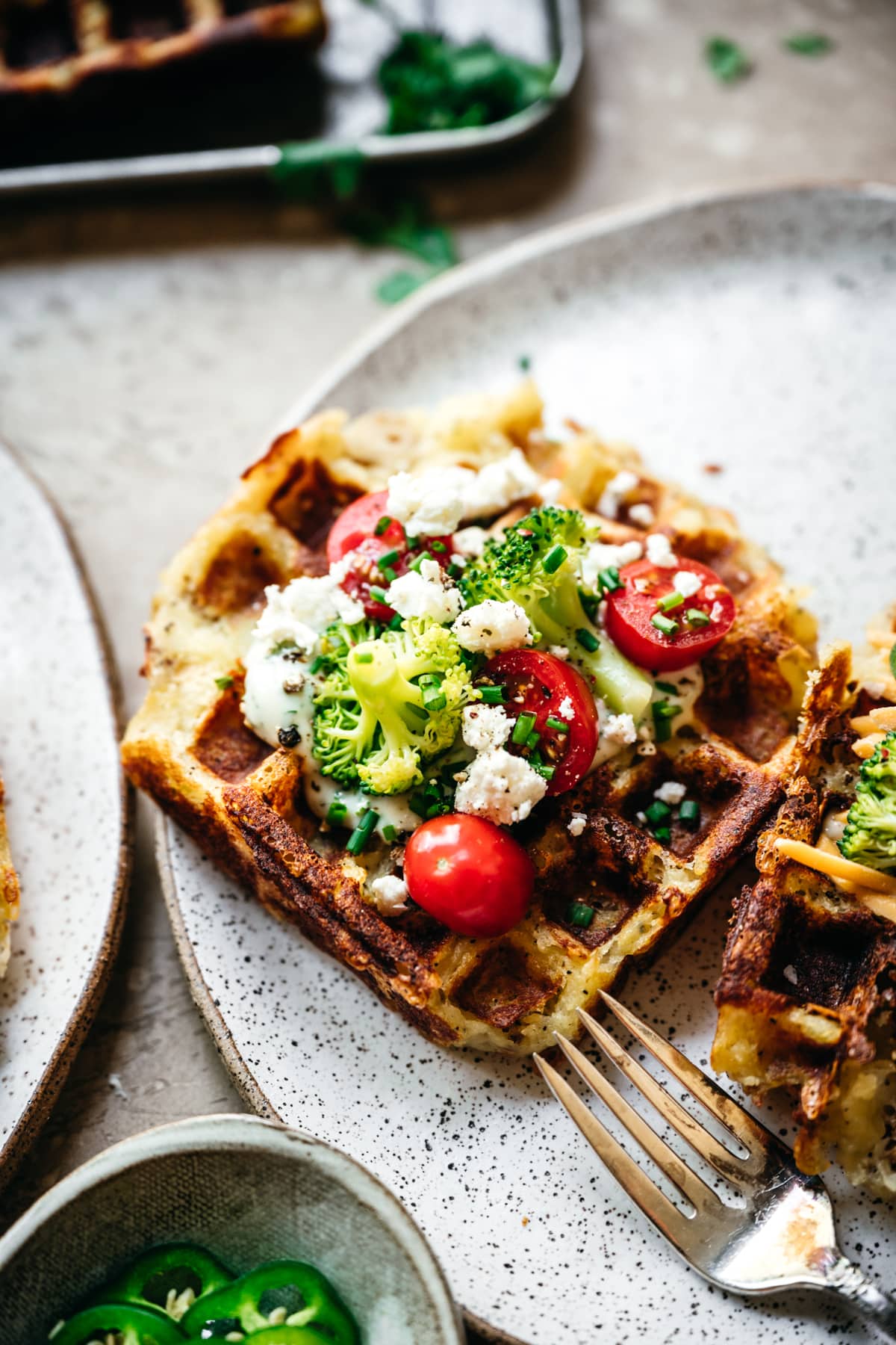 close up side view of mashed potato waffle topped with broccoli, tomatoes and cheese