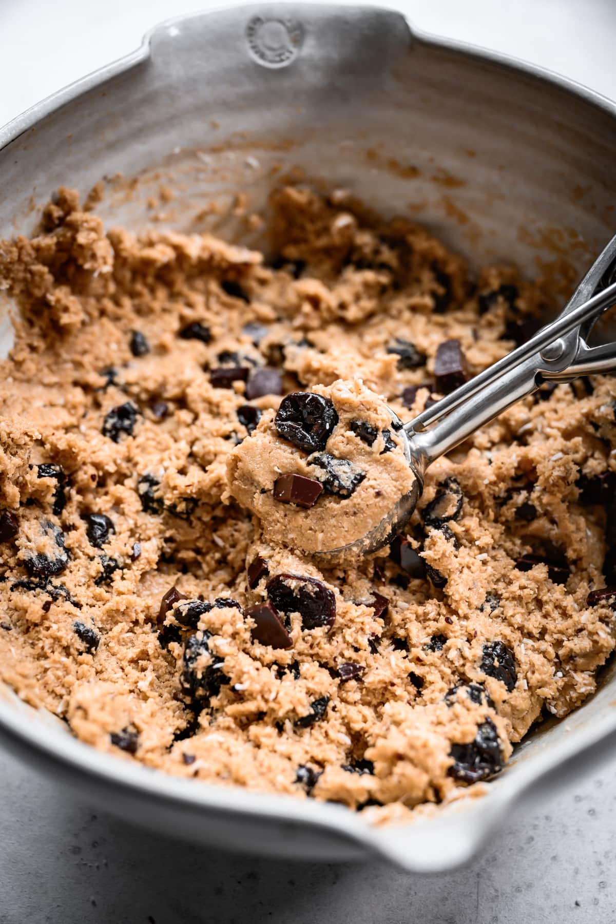 close up view of chocolate chip tart cherry cookie dough in a bowl with cookie scoop