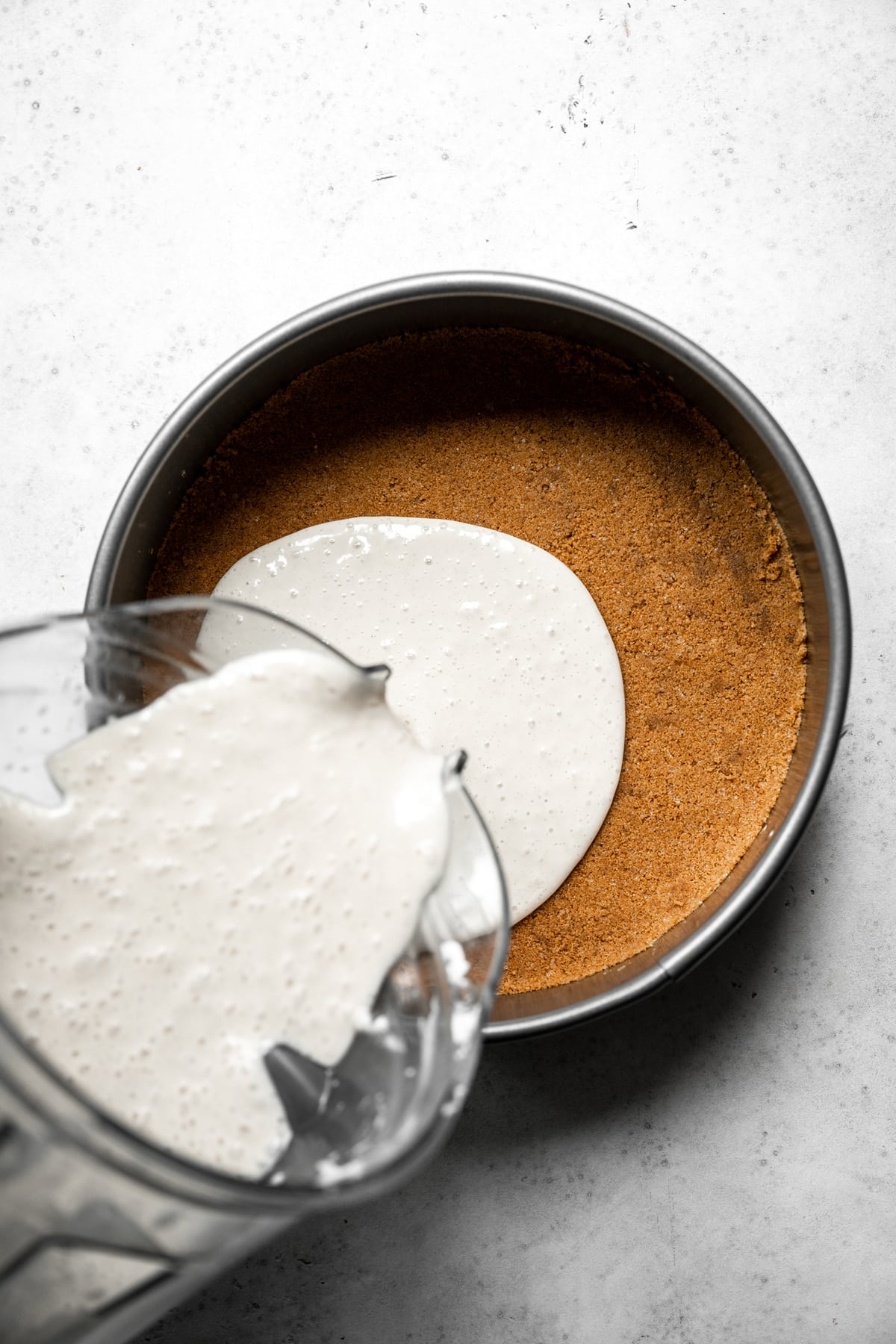 pouring vegan cheesecake filling into graham cracker crust