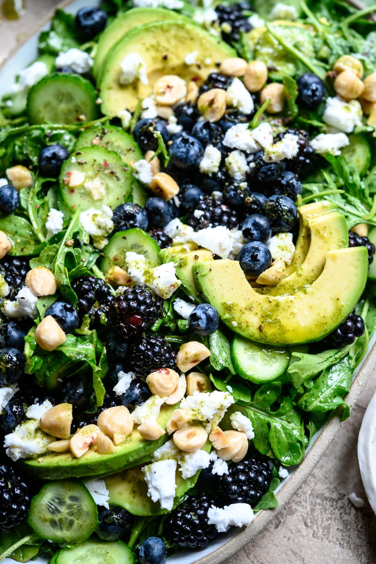 close up view of blackberry avocado arugula salad on a white platter