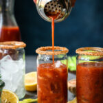 Bloody mary being poured into a glass lined with salt.