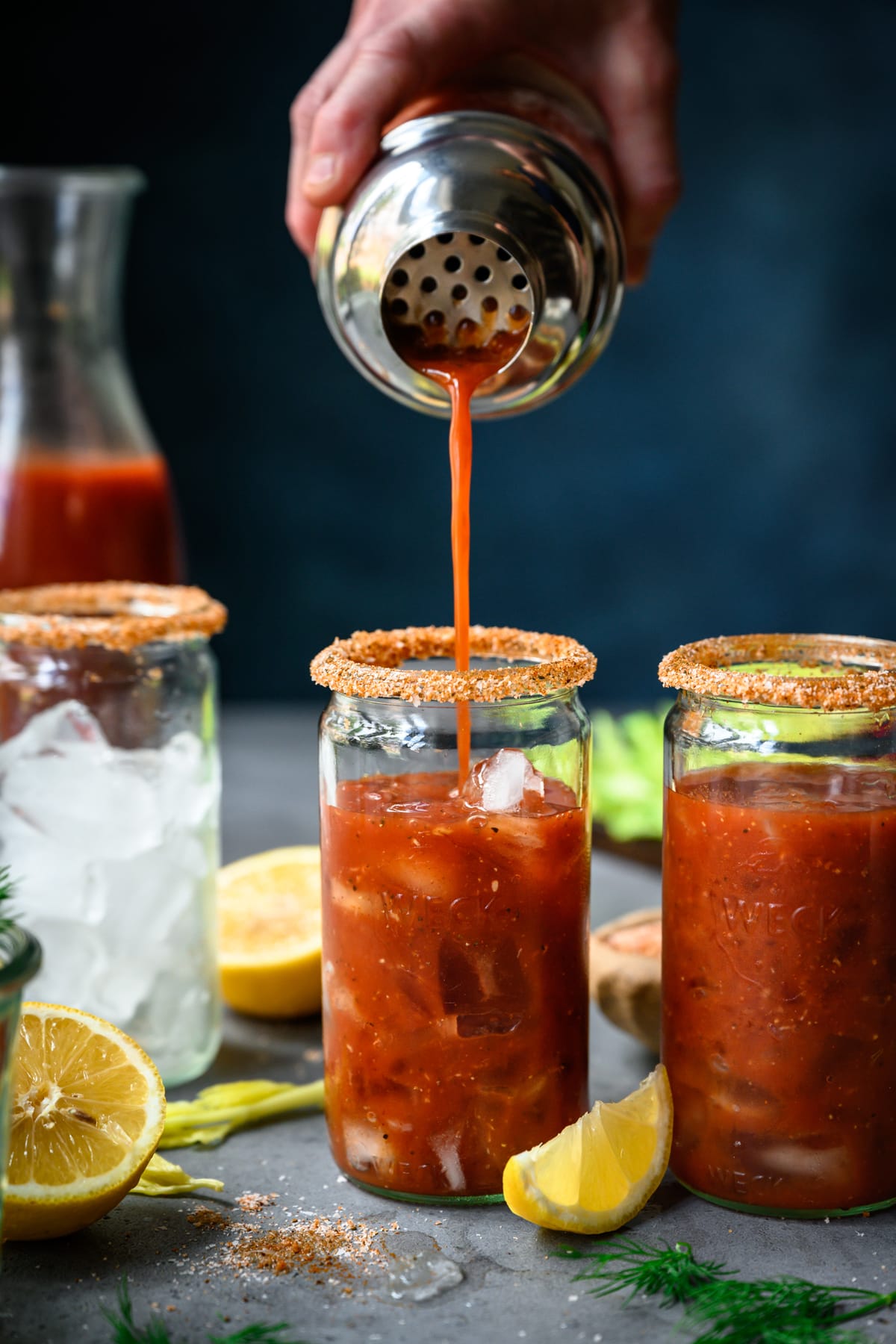 side view of pouring vegan bloody mary from cocktail shaker into glass