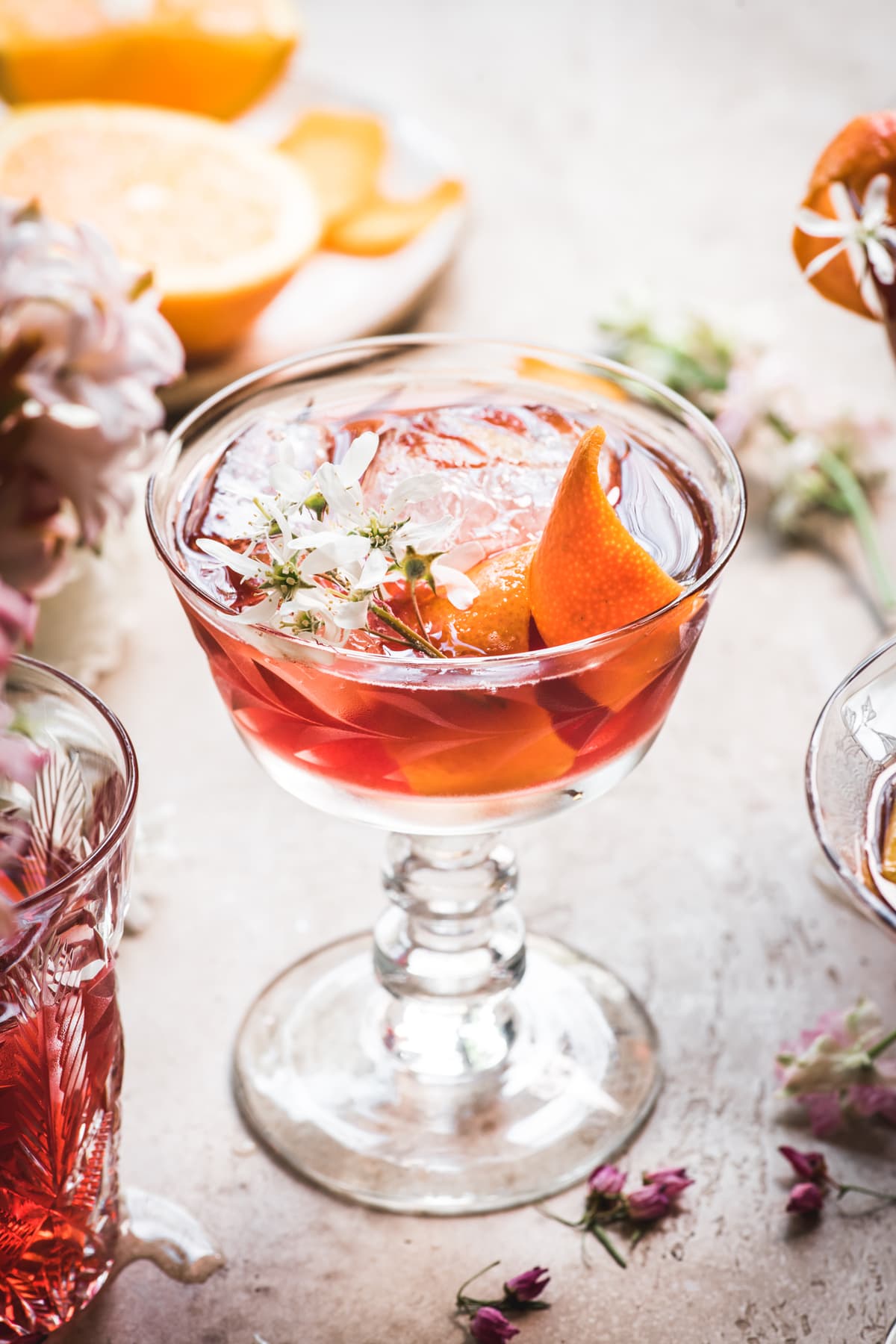 close up side view of backlit cherry negroni cocktail with orange peel and flowers