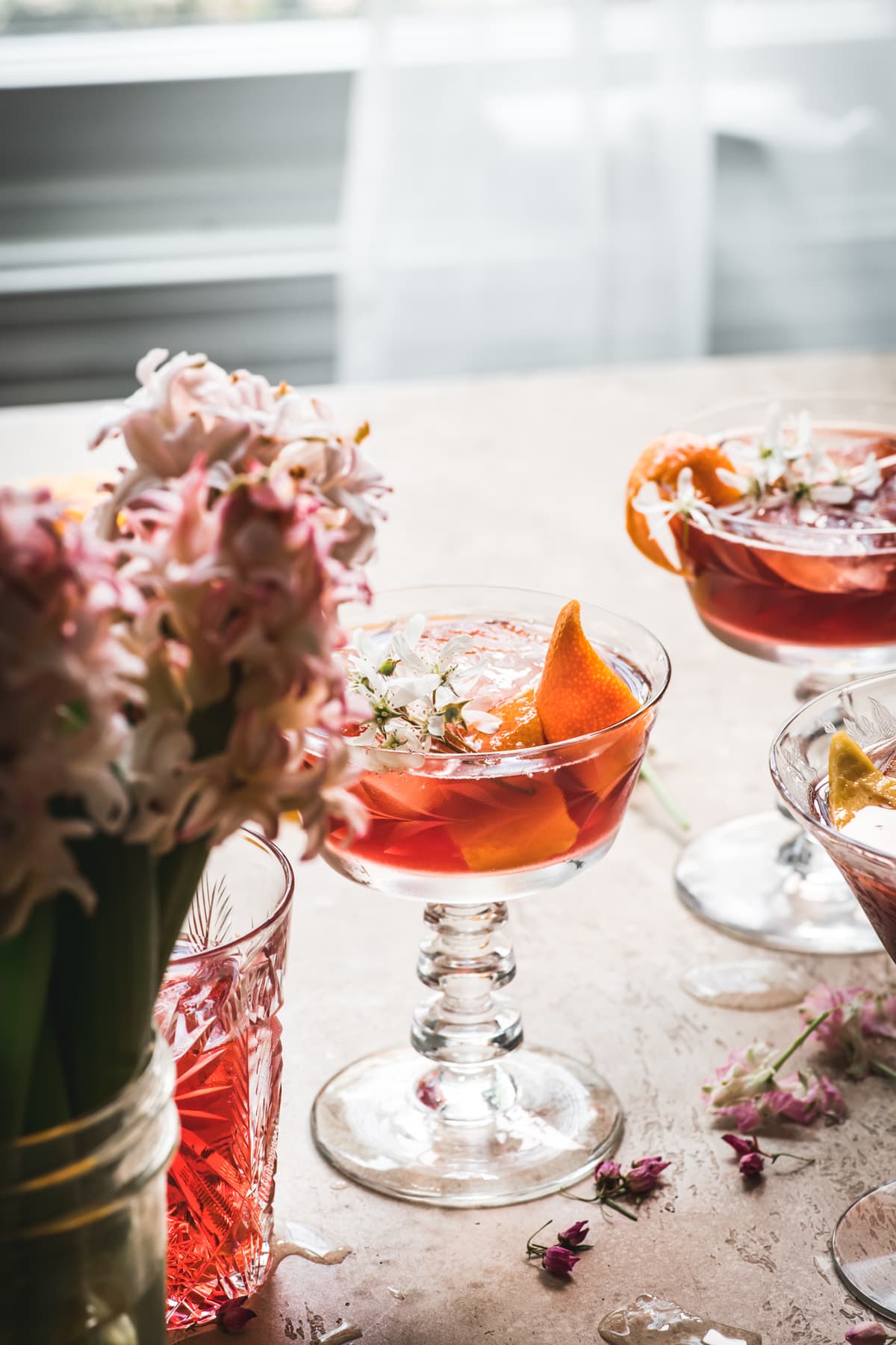 side view of backlit cherry negroni cocktail with orange peel and flowers