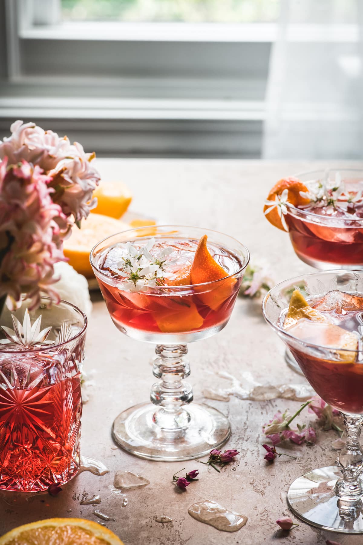 side view of backlit cherry negroni cocktail with orange peel and flowers