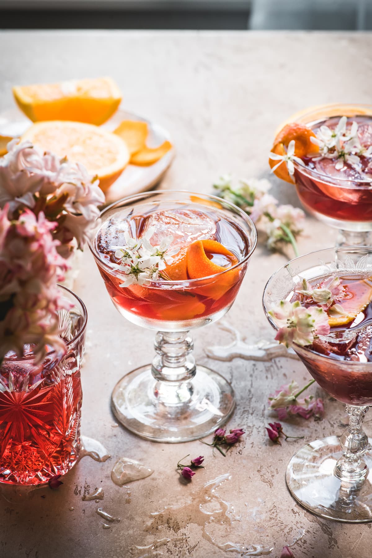 side view of backlit cherry negroni cocktail with orange peel and flowers