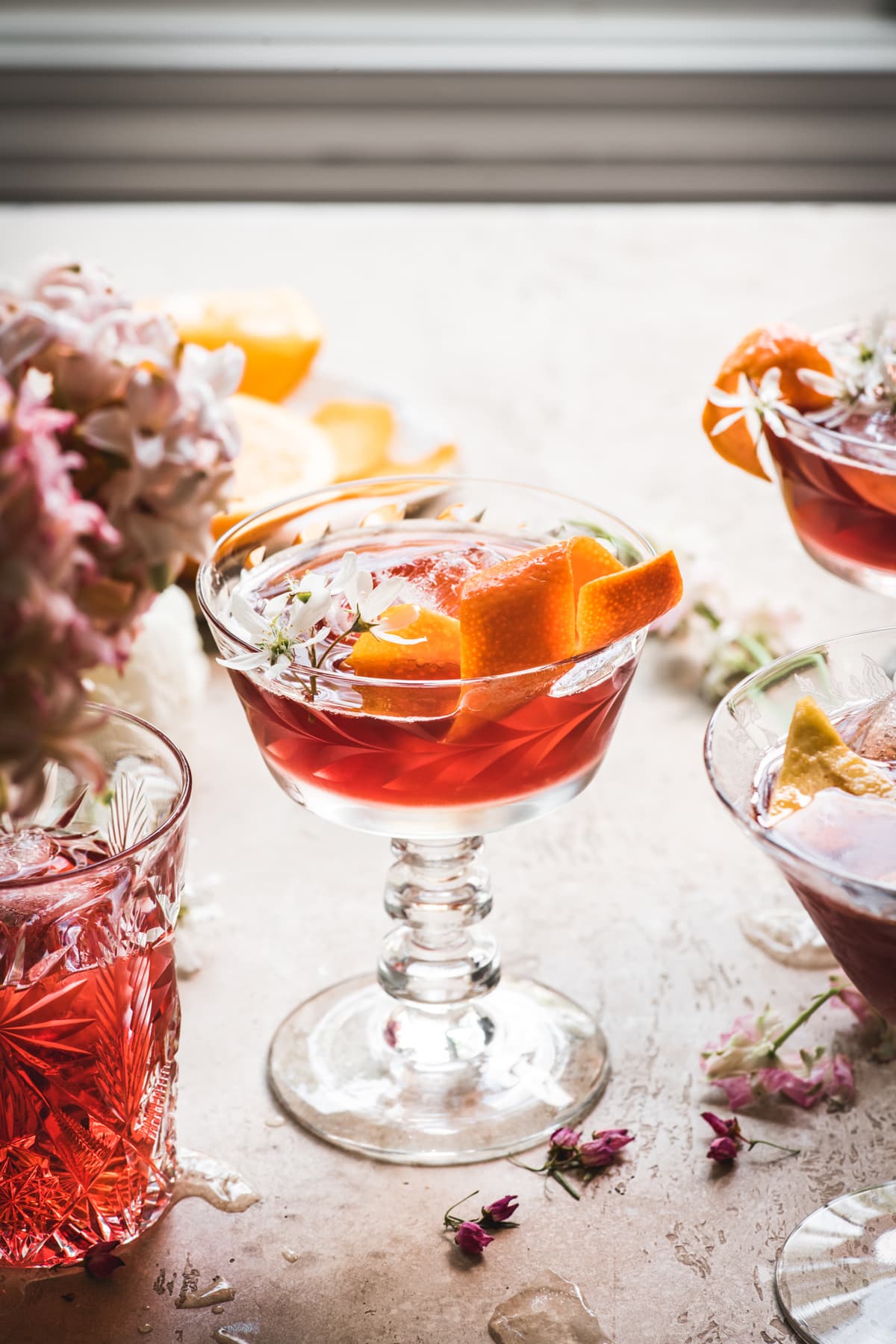side view of backlit cherry negroni cocktail with orange peel and flowers