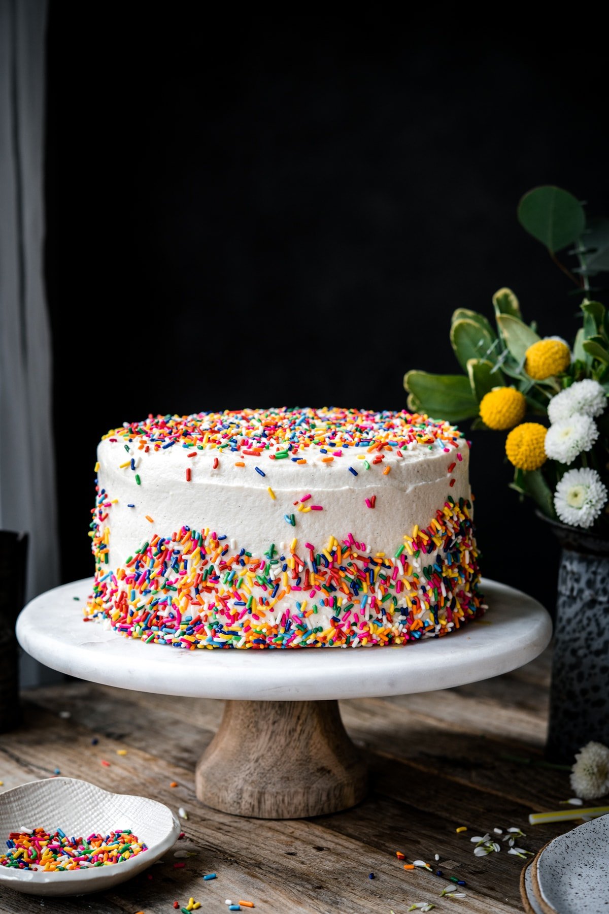 side view of vegan gluten free sprinkle cake on marble cake stand