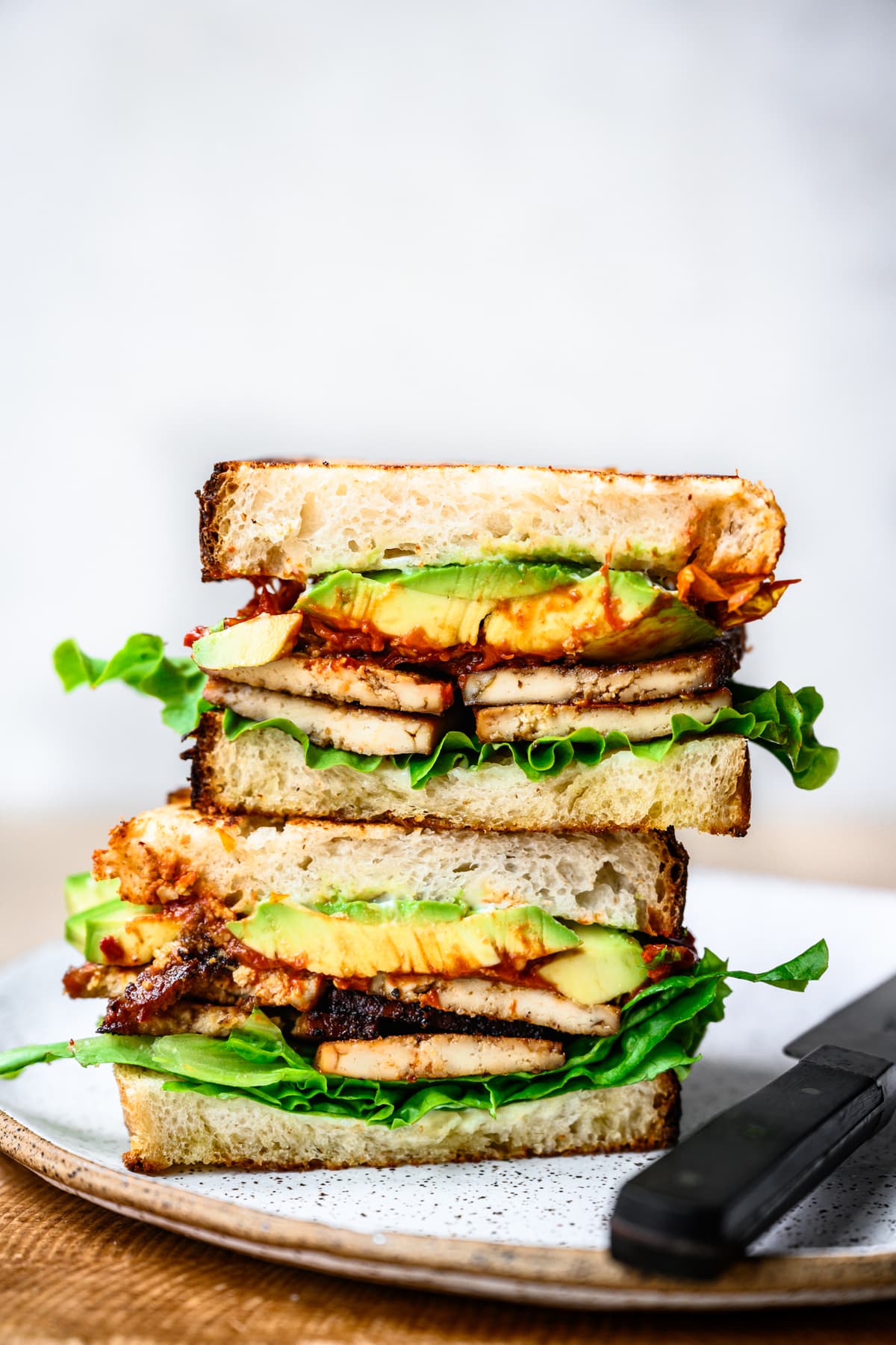 close up view of vegan BLT sandwich cut in half and stacked on plate