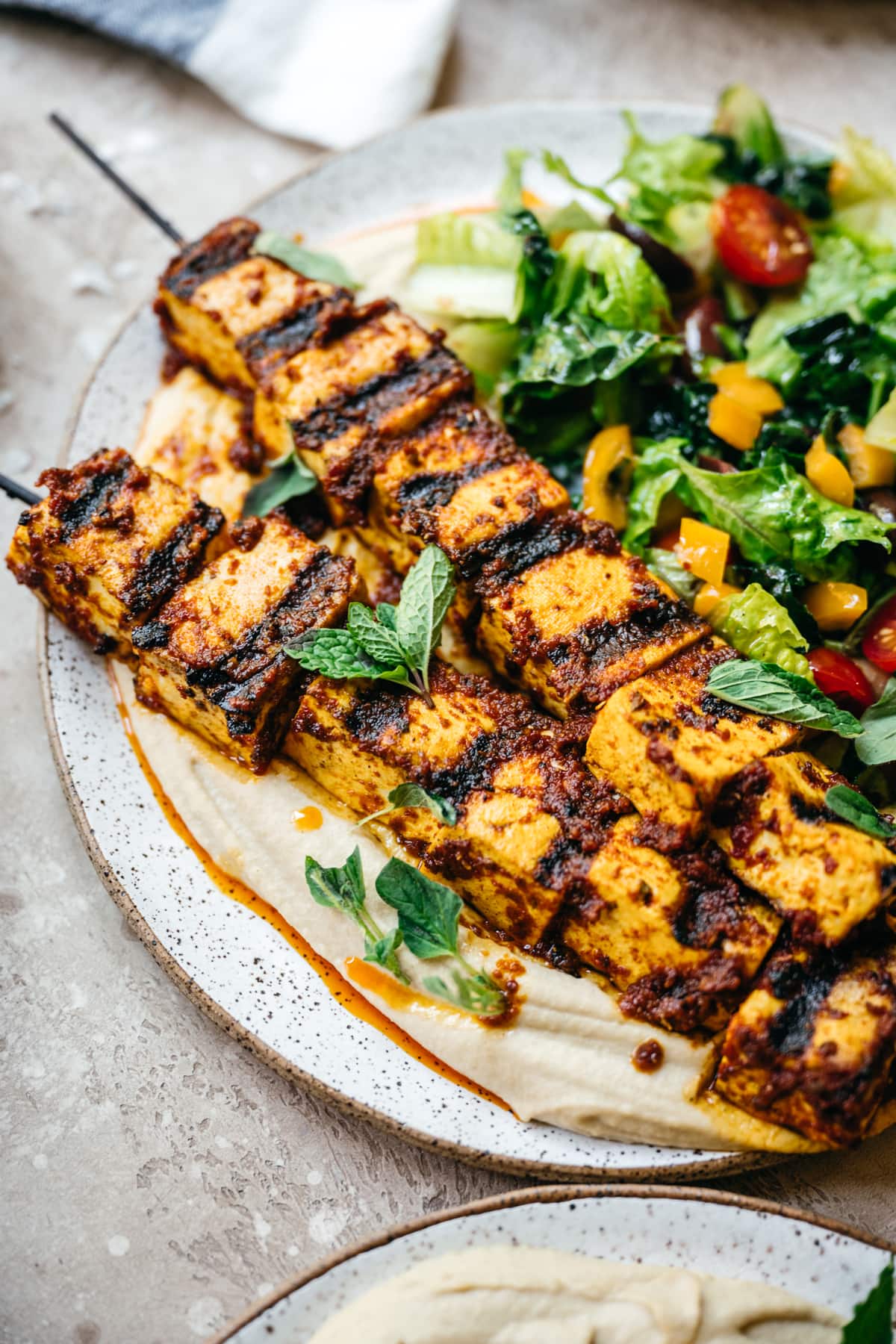 Side view of Mediterranean tofu kebabs over hummus with a salad