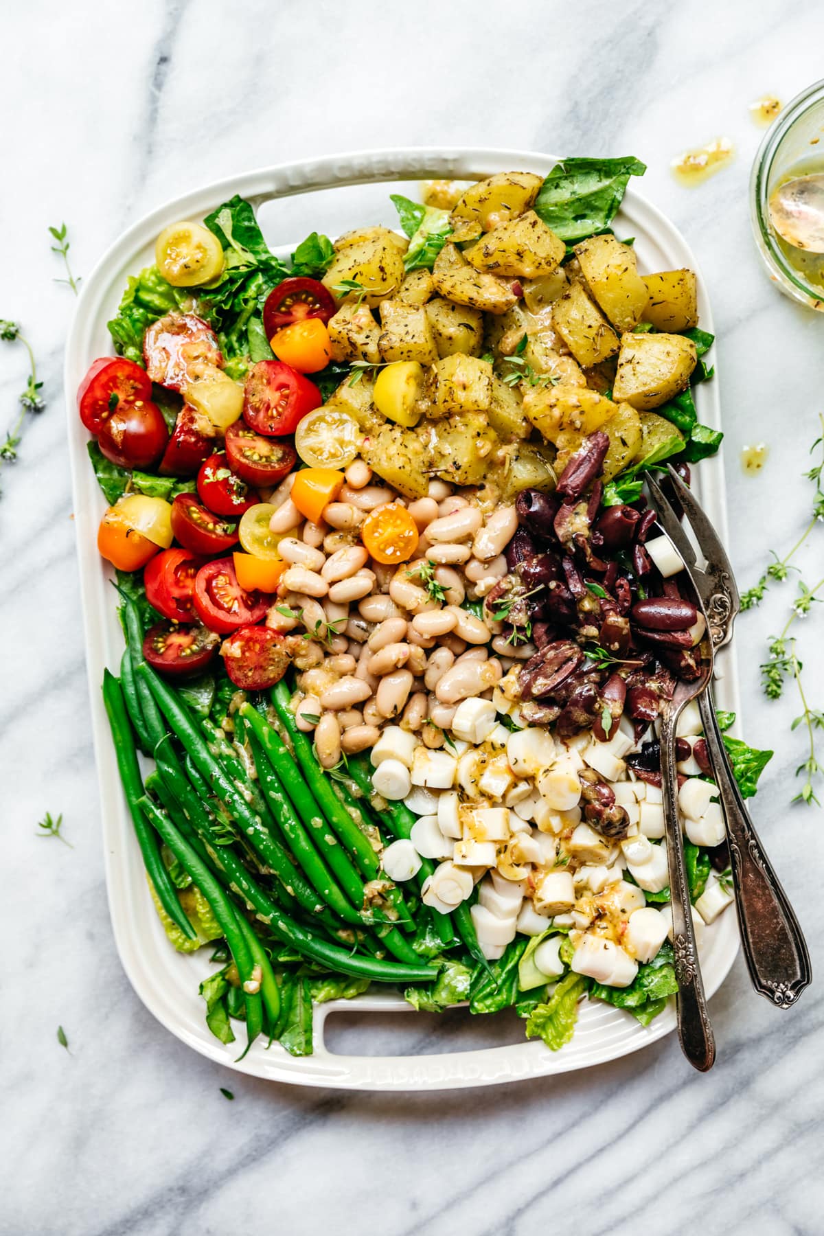 overhead view of vegan nicoise salad with white beans on a white platter