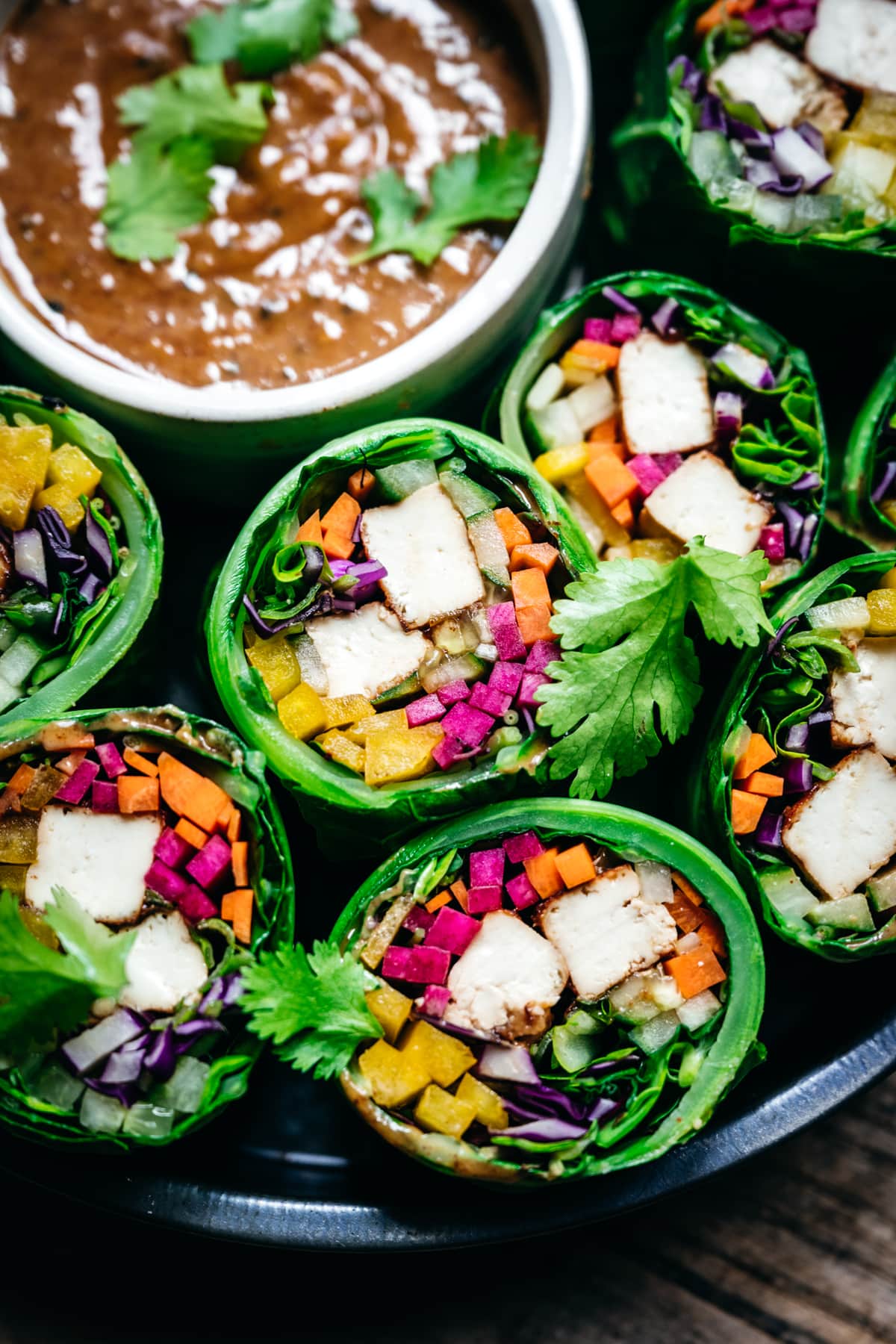 Close up view of vegan collard green wraps with vegetables and tofu cut in half with almond miso sauce