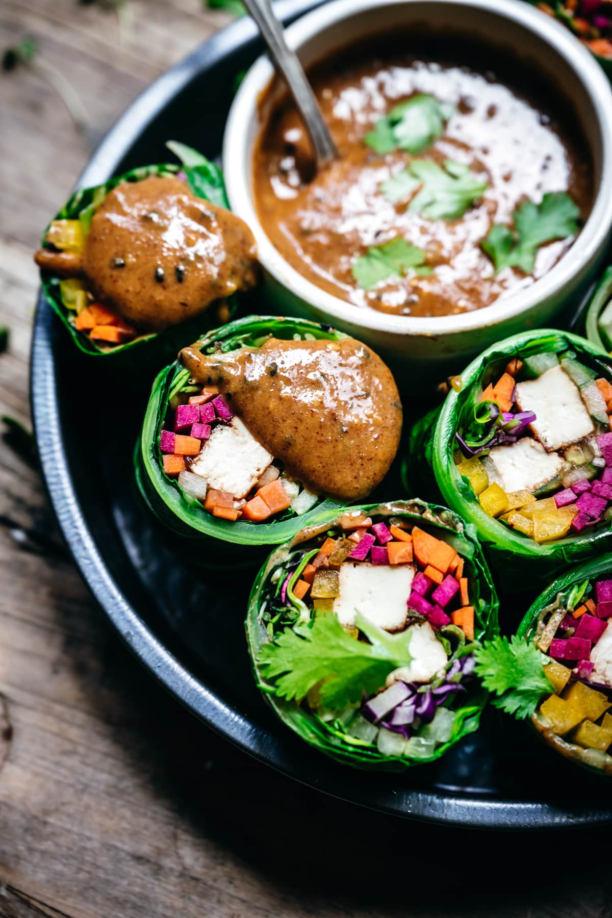 close up view of vegan collard green wraps with vegetables and tofu cut in half with almond miso sauce